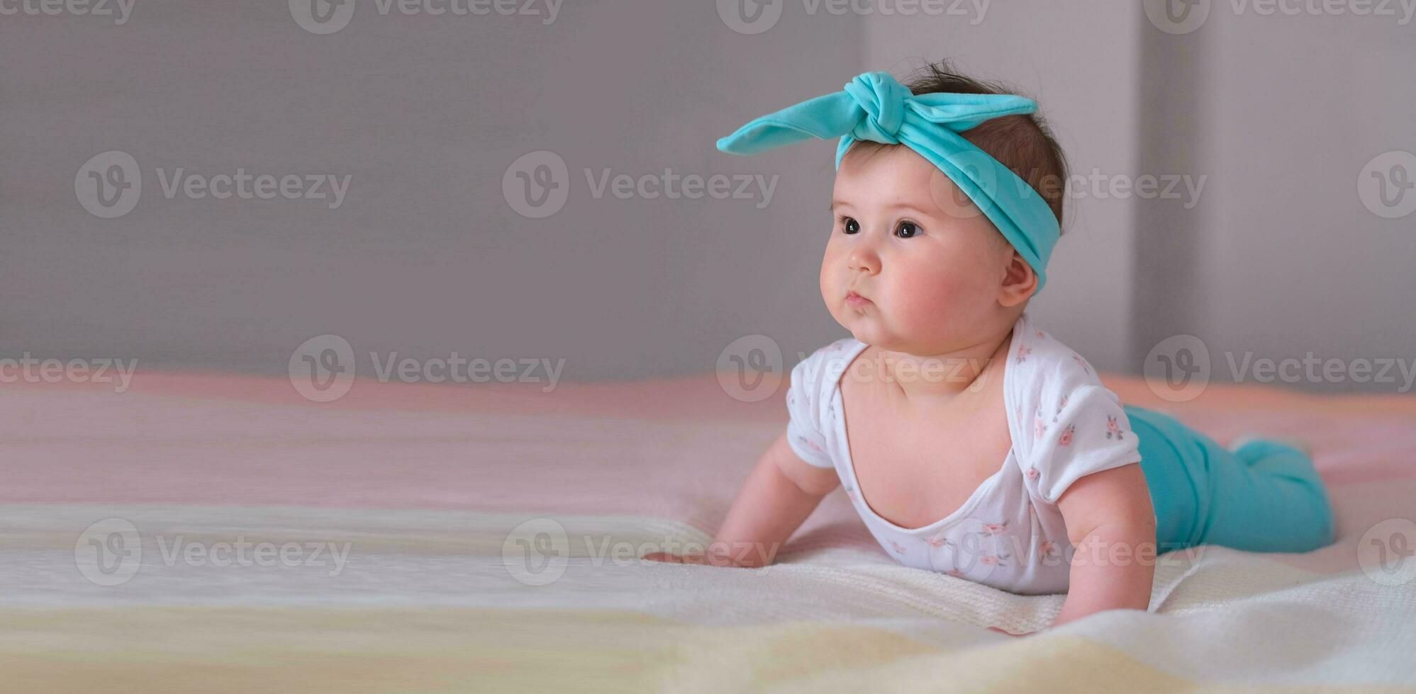 Banner. Baby at 6 months raises his body and learns to crawl. A little girl lies on her stomach on the bed. A beautiful headband for a child. photo