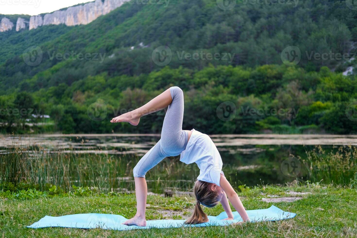 A little girl makes a bridge, bending her back in nature. A flexible child, doing gymnastics exercises. Sports, learning, fitness, stretching, yoga, active lifestyle concepts photo
