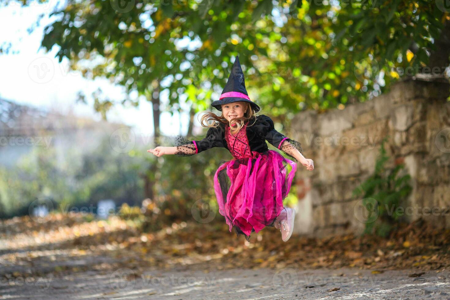 A little girl in a witch costume is jumping on the street. Halloween holiday. Copy space photo
