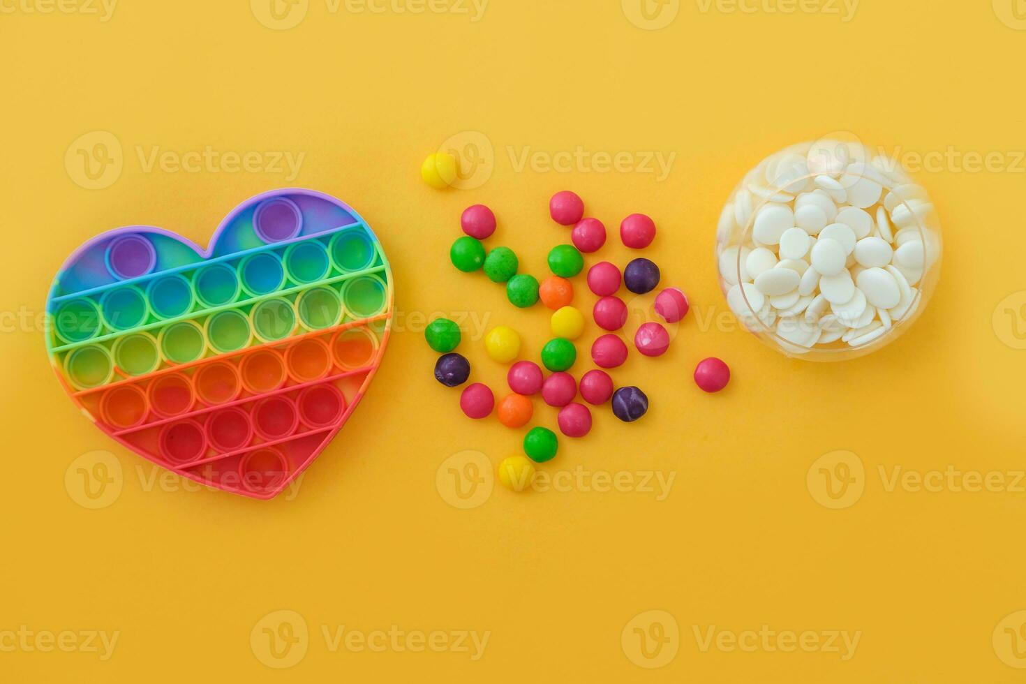 Use the popular pop it toy as a chocolate mold. White chocolate, colorful candies and popit heart-shaped silicone mold on yellow background. DIY concept. Step-by-step photo instructions. Step 1.