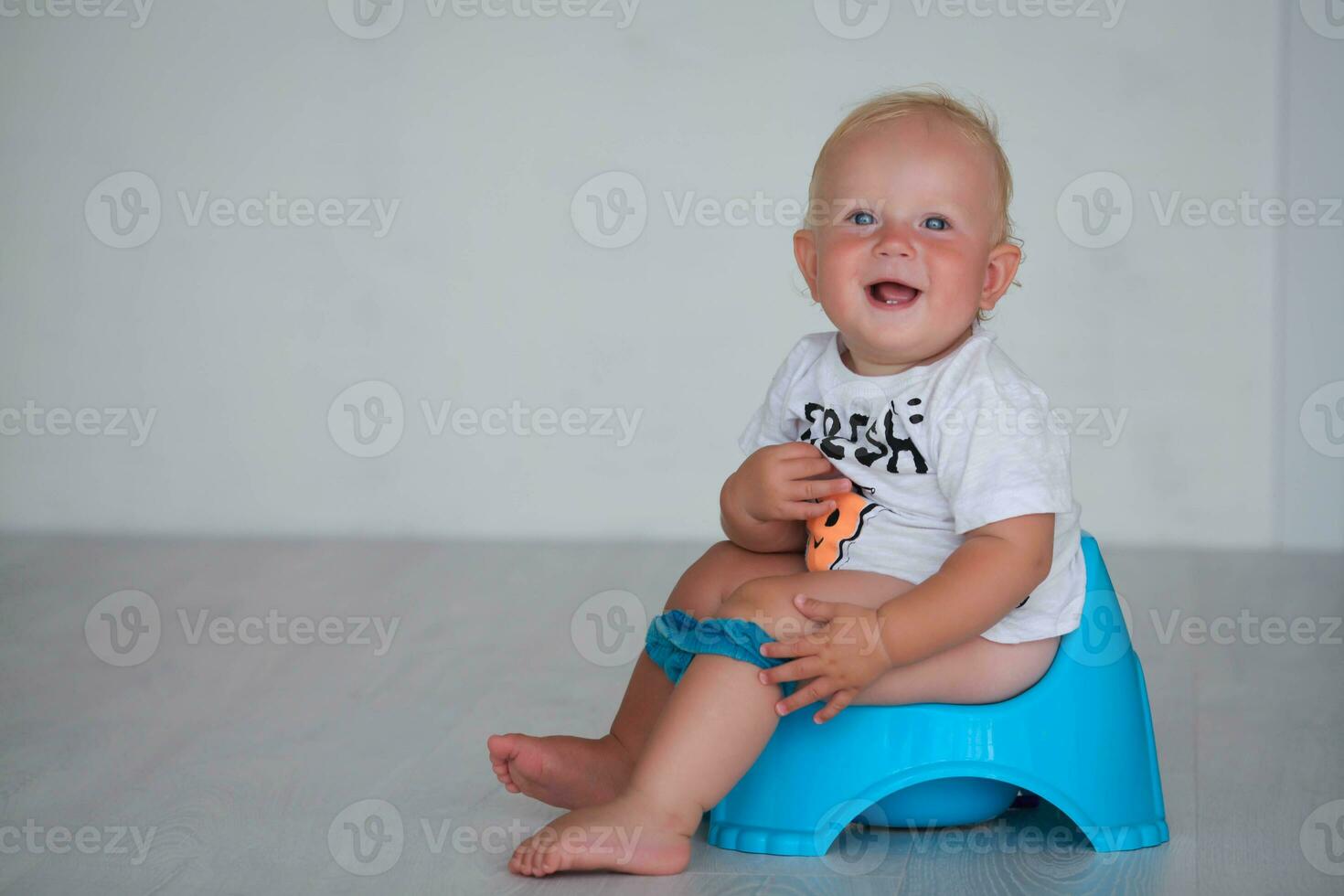 Little boy sits on a blue pot. The baby looks at the camera and smiles at the pot. photo