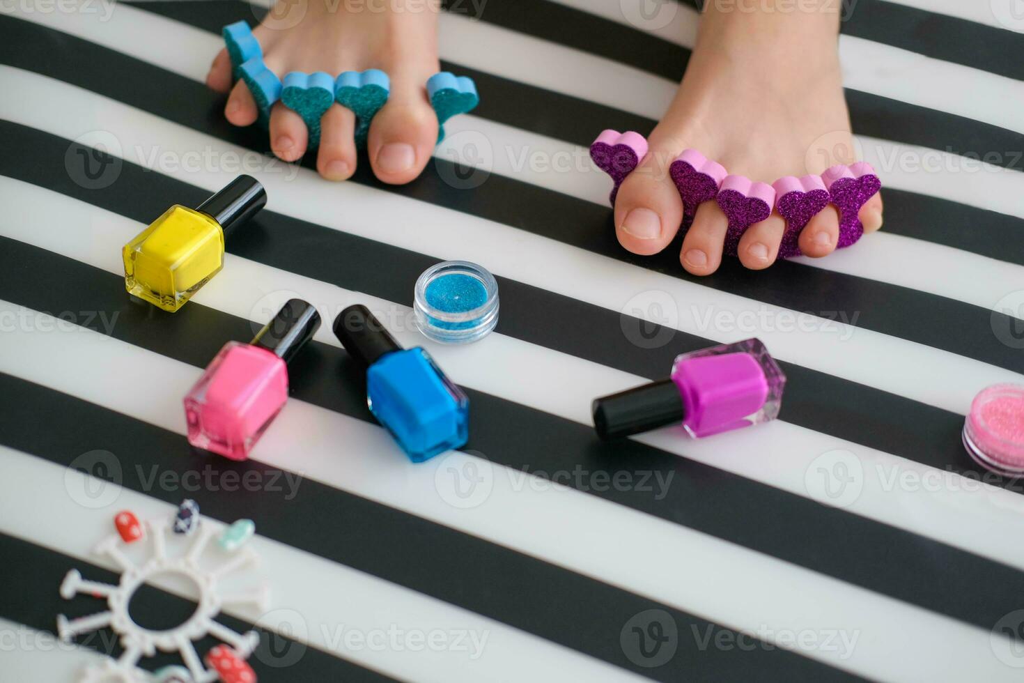 Baby feet with bright pedicure of different colors and bottles of bright nail polish. Little girl does a pedicure. Beauty salon game. Children's entertainment. photo