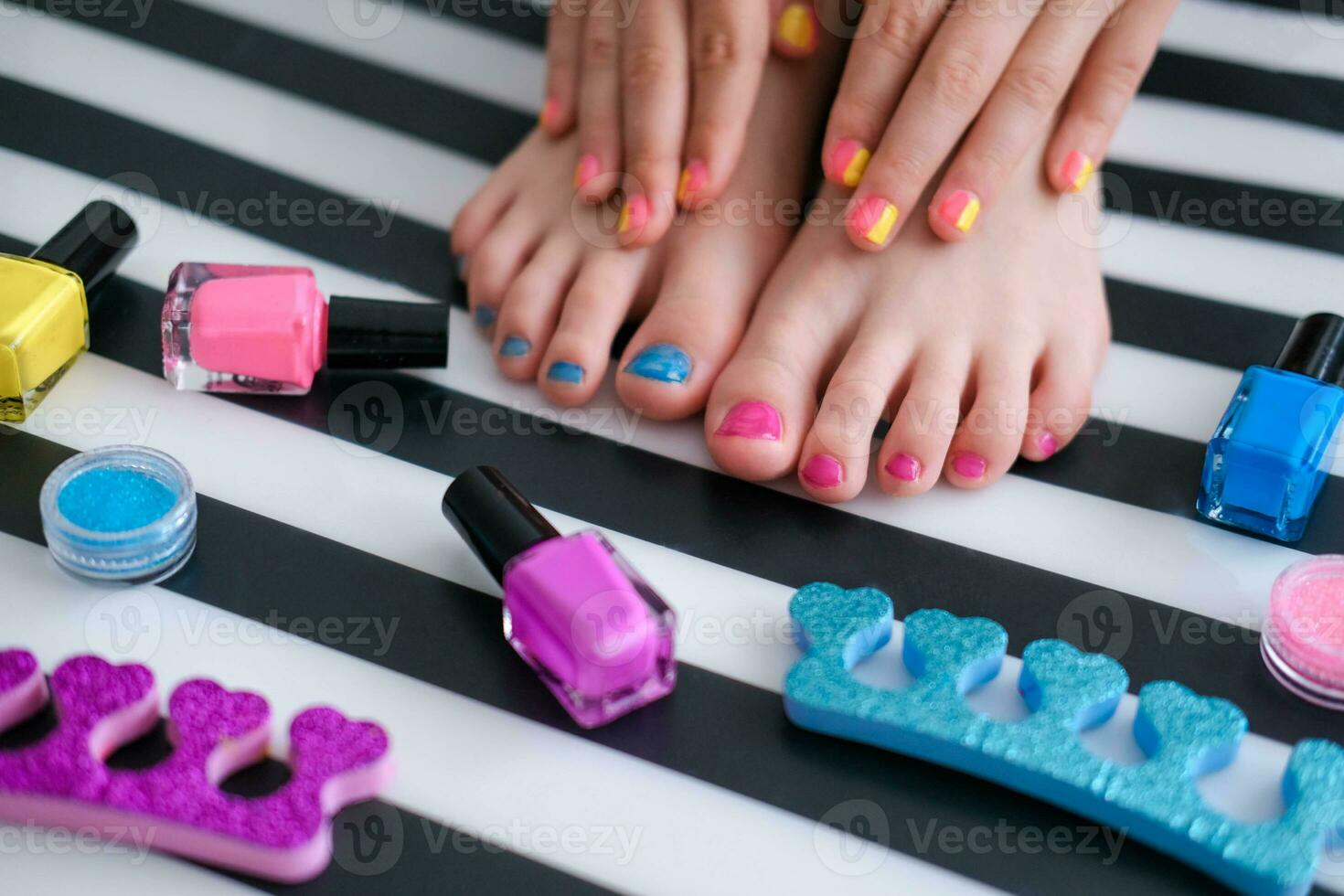 Children's feet with bright pedicure and manicure of different colors and bottles of bright nail polish. Little girl does a pedicure. Beauty salon game. Children is entertainment. photo