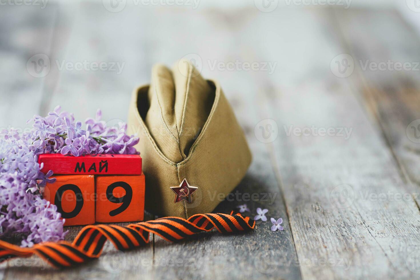 Wooden calendar with Russian text May 9, garrison cap, george ribbon and a bouquet of lilacs on a wooden background. Victory Day. photo
