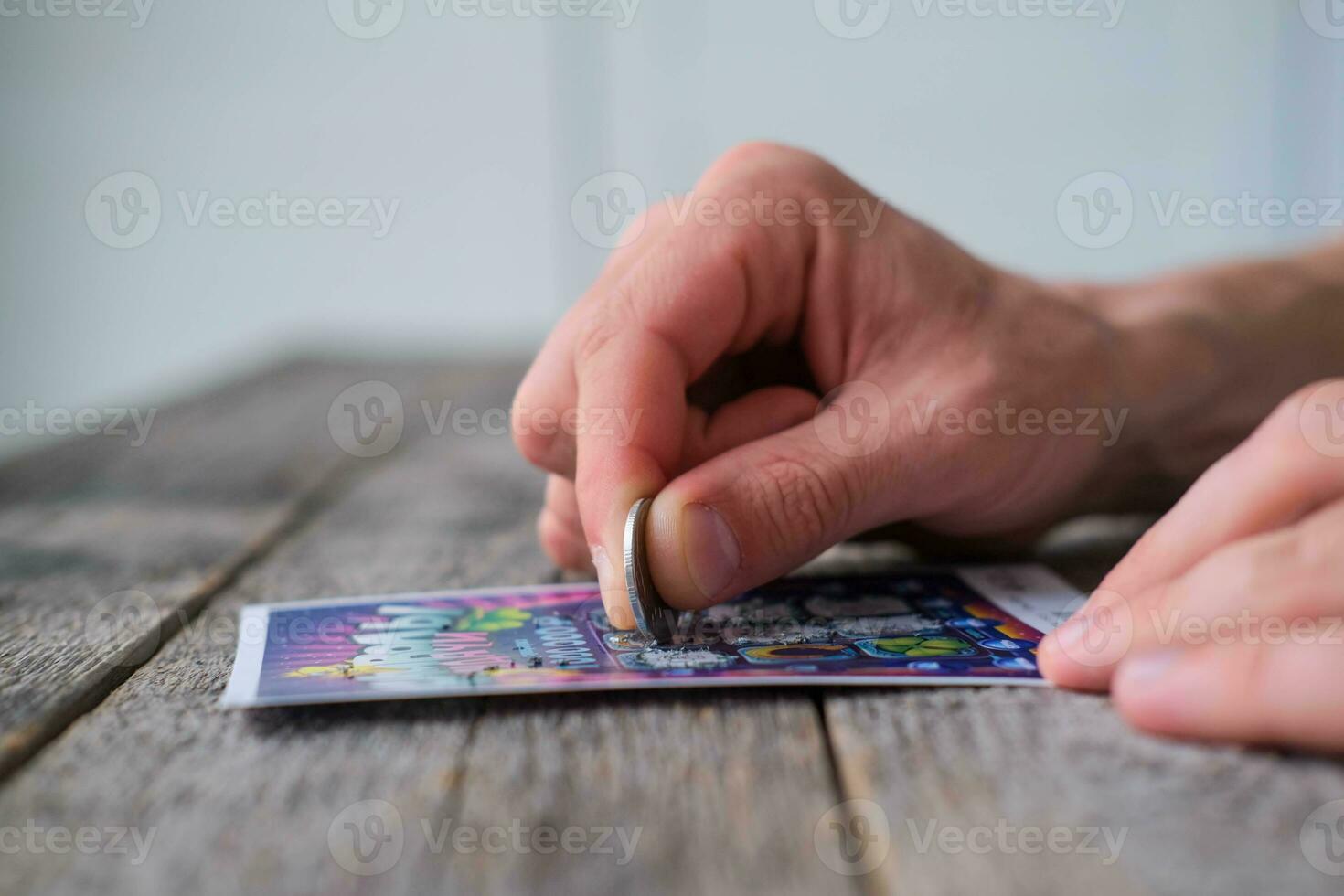 A man is hand erases a protective field in a lottery with a coin on a wooden background. Won. Gambling, addiction. photo