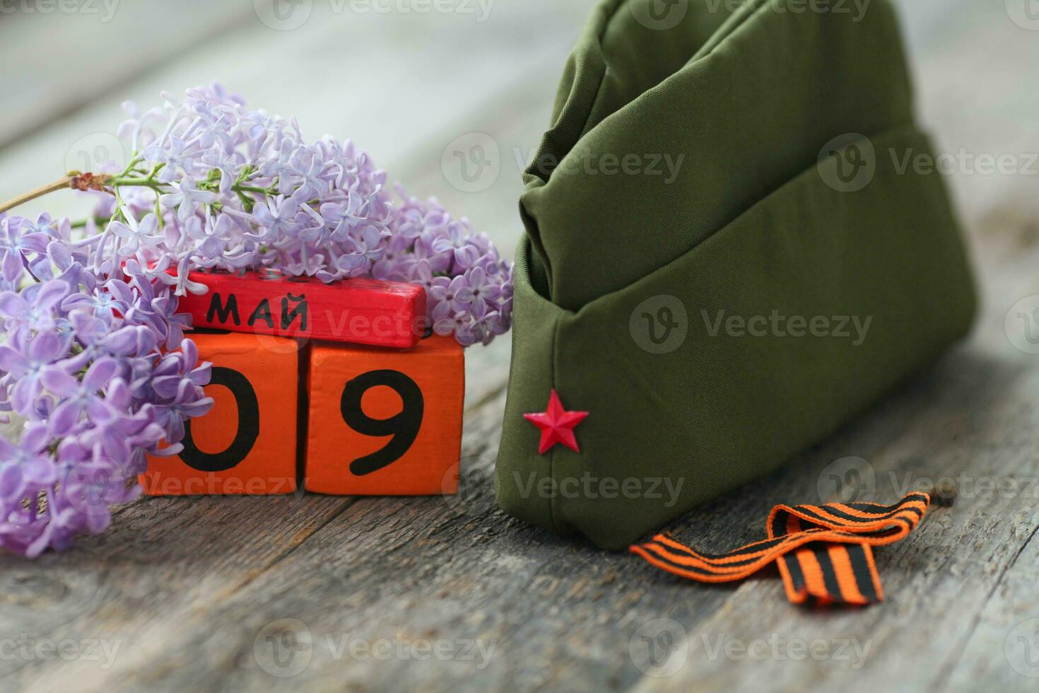 Wooden calendar with Russian text May 9, garrison cap, george ribbon and a bouquet of lilacs on a wooden background. Victory Day. photo