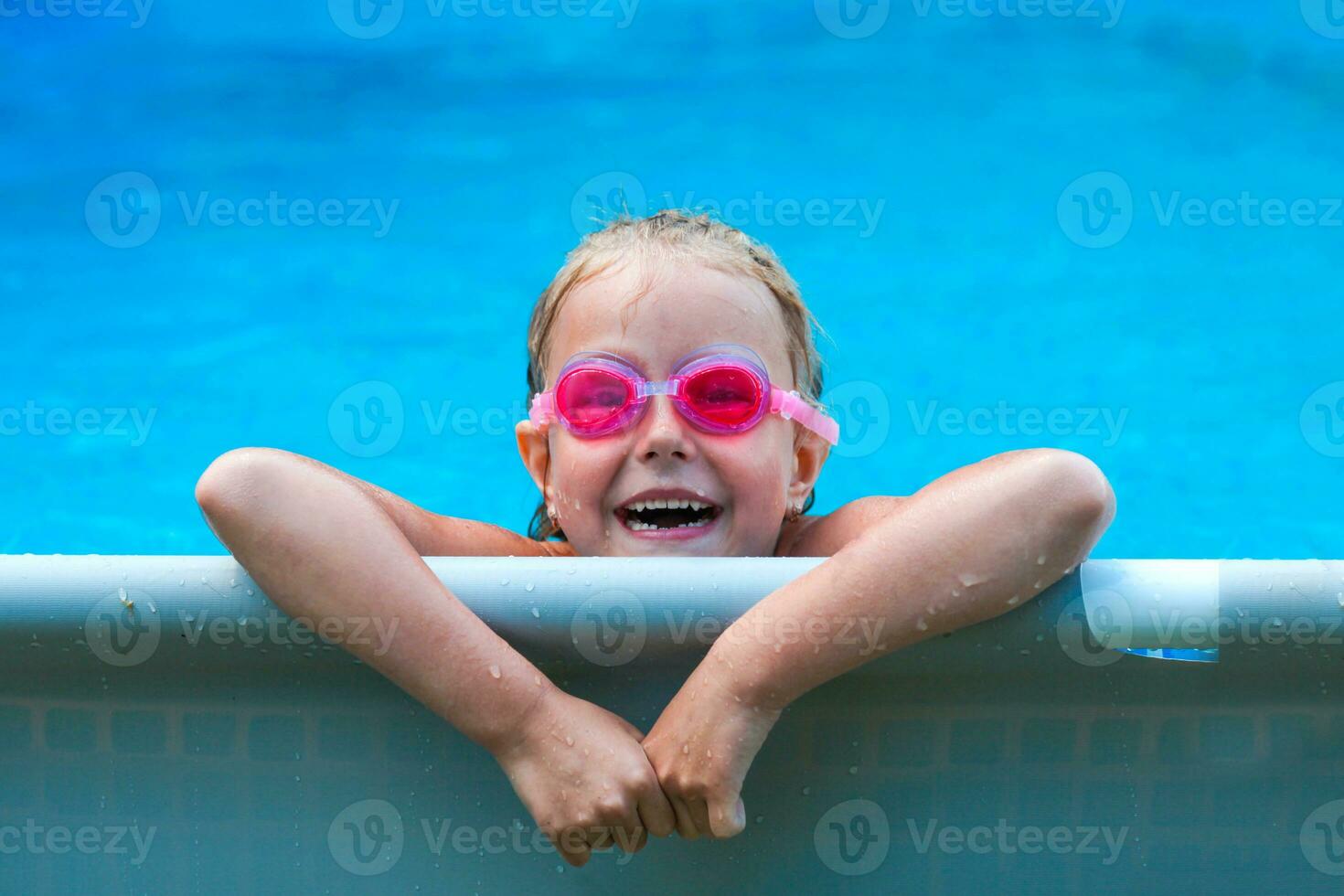 Cute little girl smiling in goggles in the pool on a sunny day. The child looking camera . Summer vacation photo