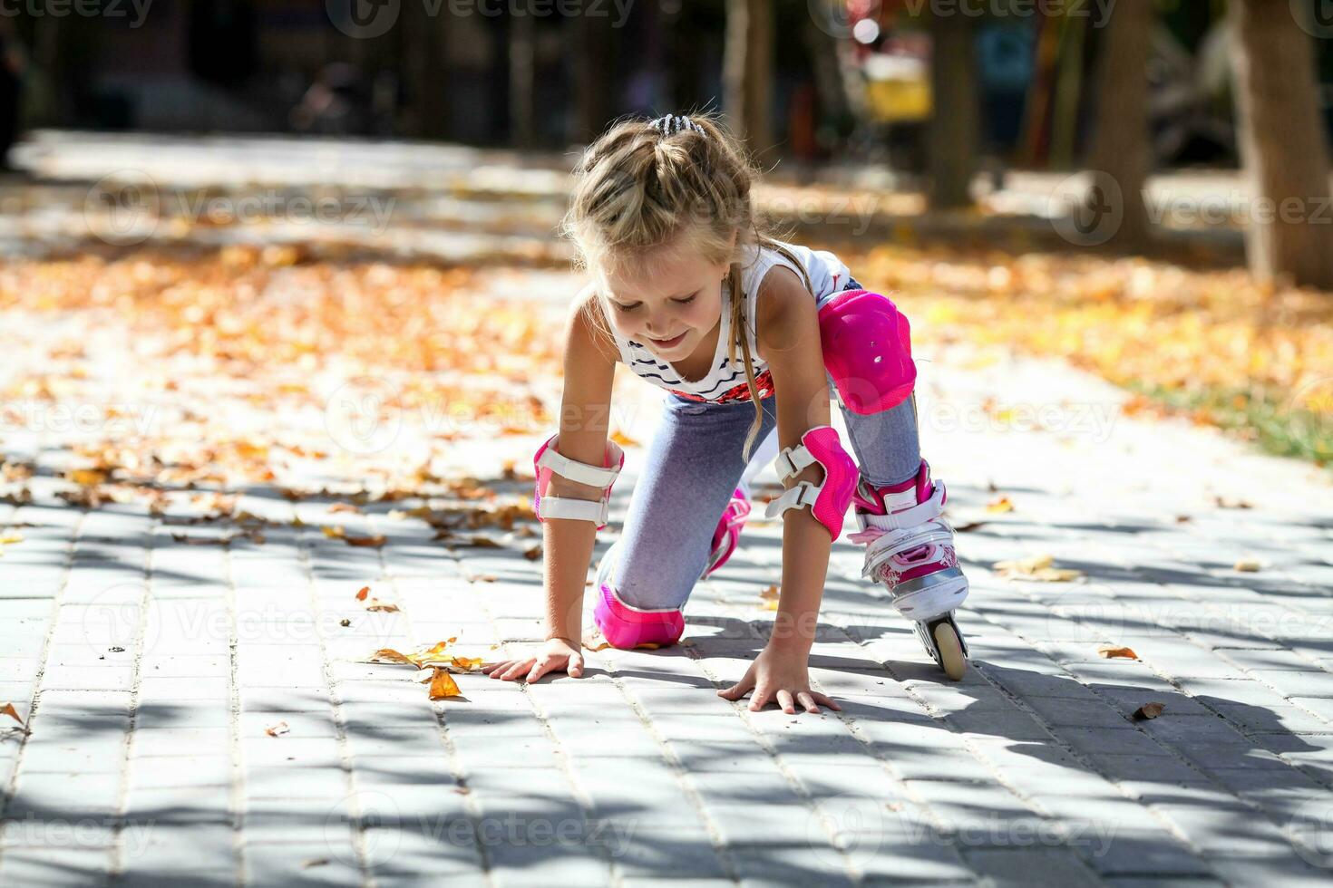 un pequeño niña en rodillo patines y proteccion cayó a el suelo en un otoño parque. foto