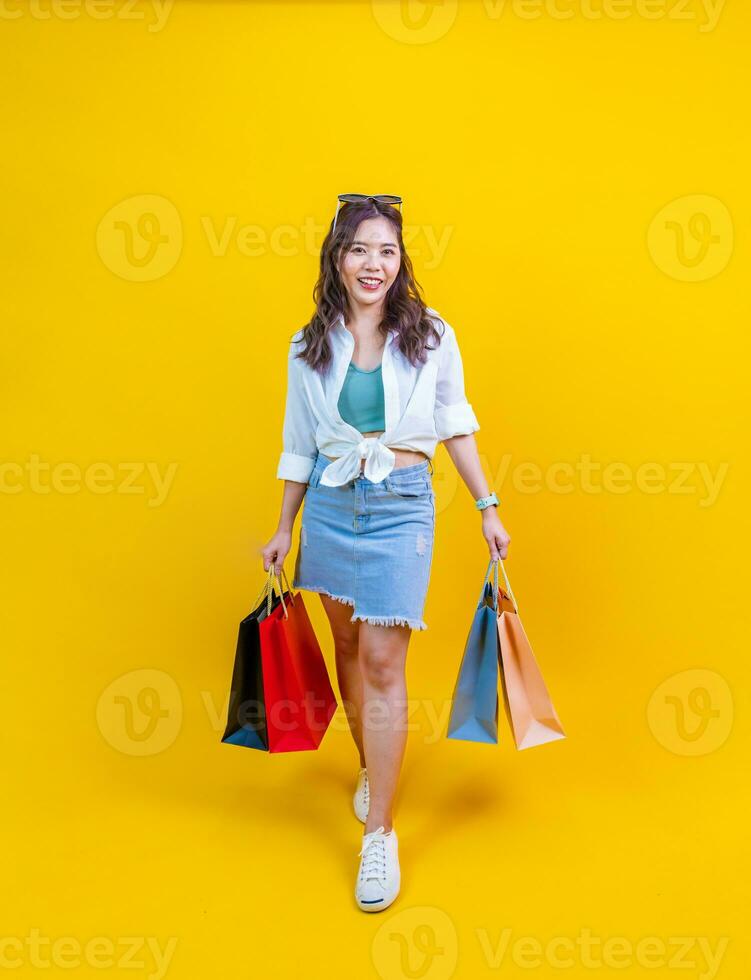 bonito asiático mujer en de moda verano Moda es sonriente y participación compras pantalones en felicidad para descuento rebaja aislado en amarillo antecedentes para publicidad y promoción evento concepto foto