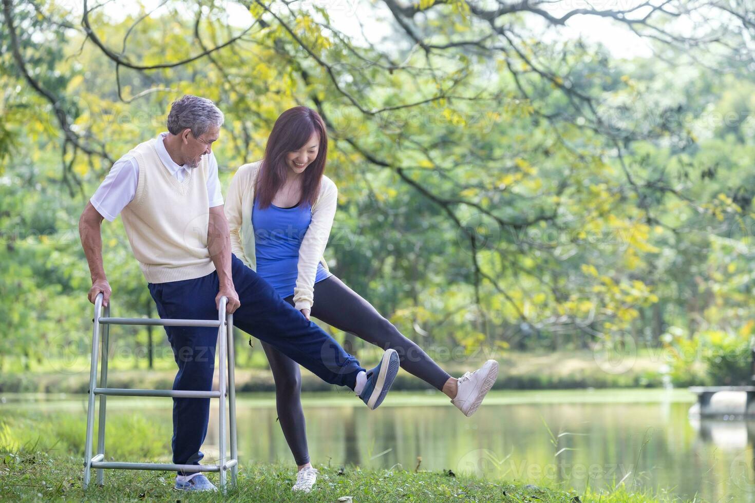 Asian senior man with walker and his daughter walking together in the park doing light exercise and physical therapy for muscle building in longevity and healthy lifestyle after retirement concept. photo