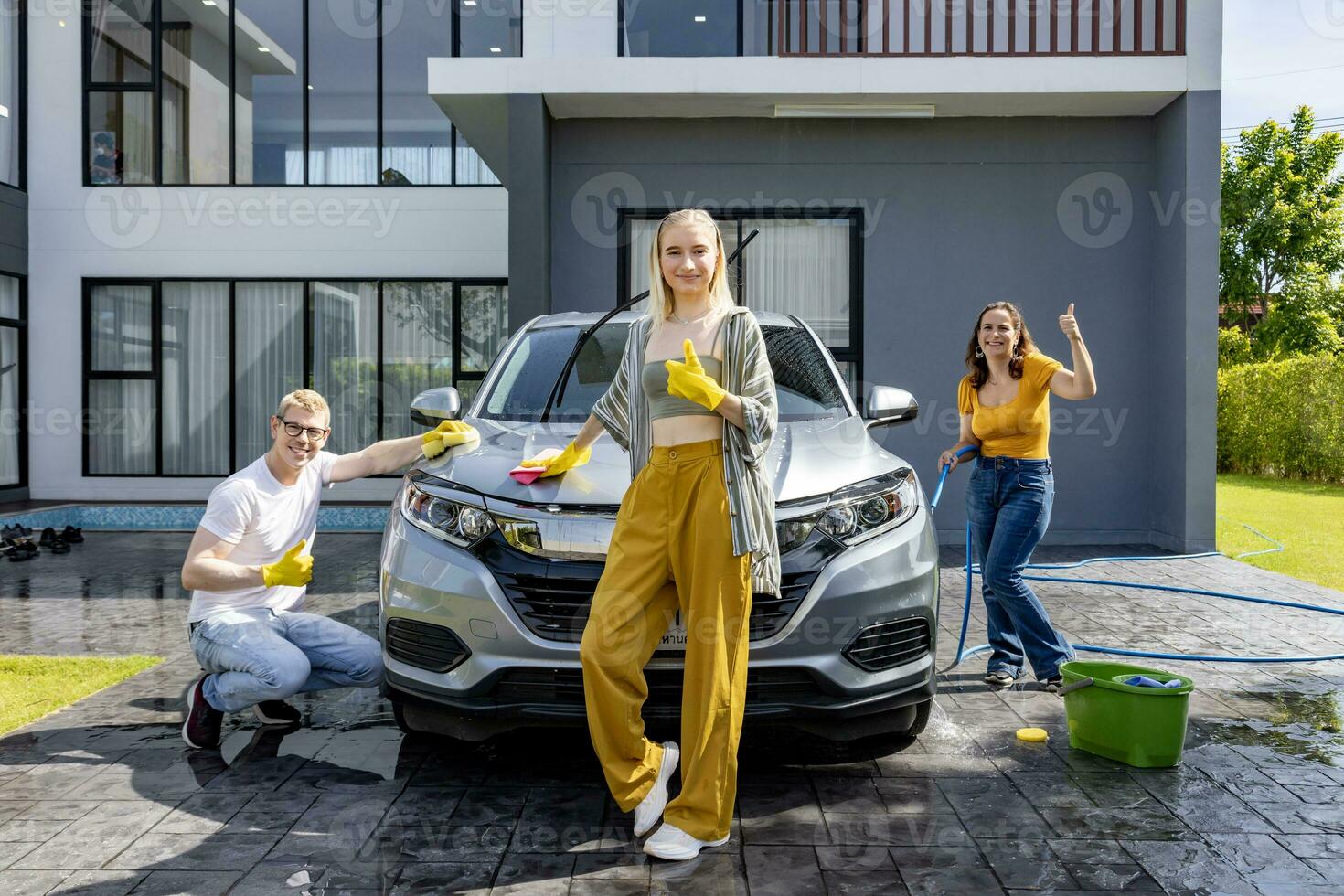 Caucasian family is smiling while helping each other using sponge and soap water to wash their car in the backyard garage during weekend for moment of quality time and activities at home concept. photo