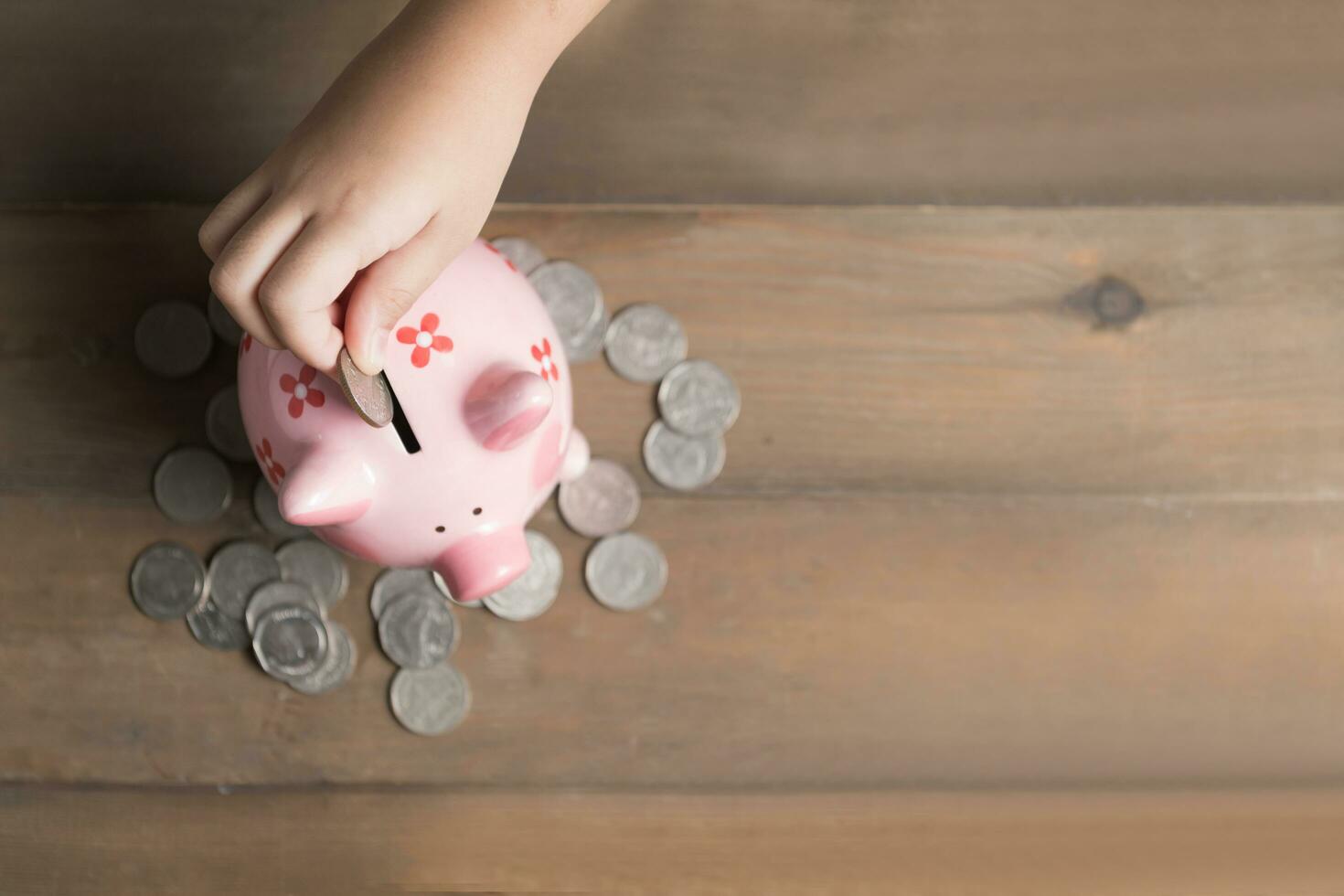 kid put coin to piggy bank on the vintage wood photo