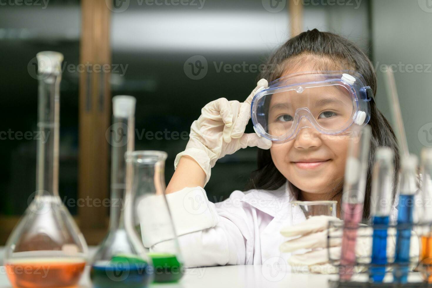 Cute little girl wearing safty goggle and lab coat making experiment photo