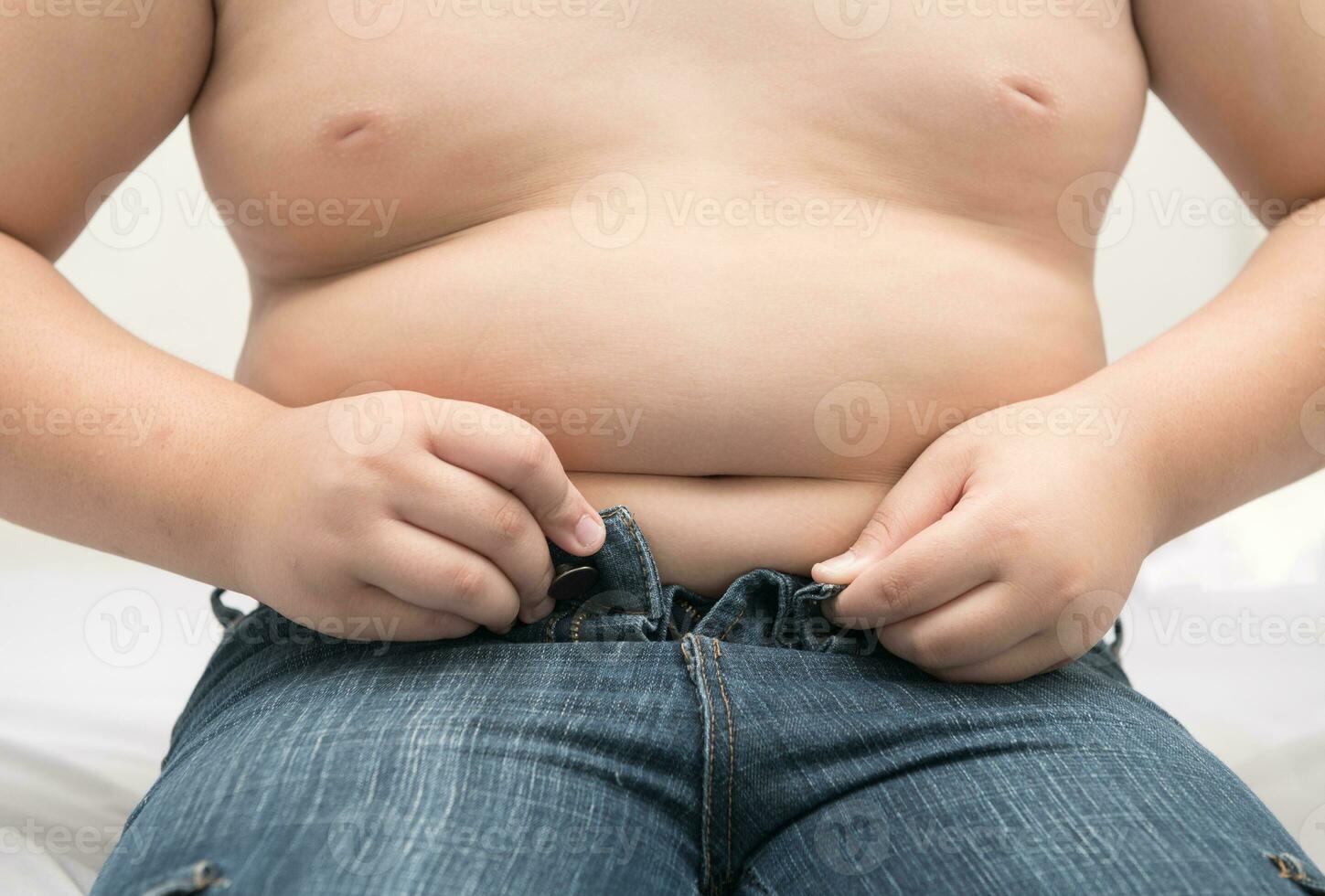 Obese fat boy try to wear jeans on bed. photo
