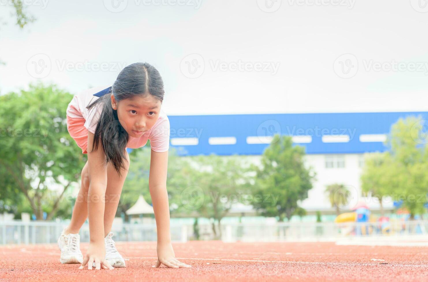 Cheerful cute girl in ready position to run on track, photo