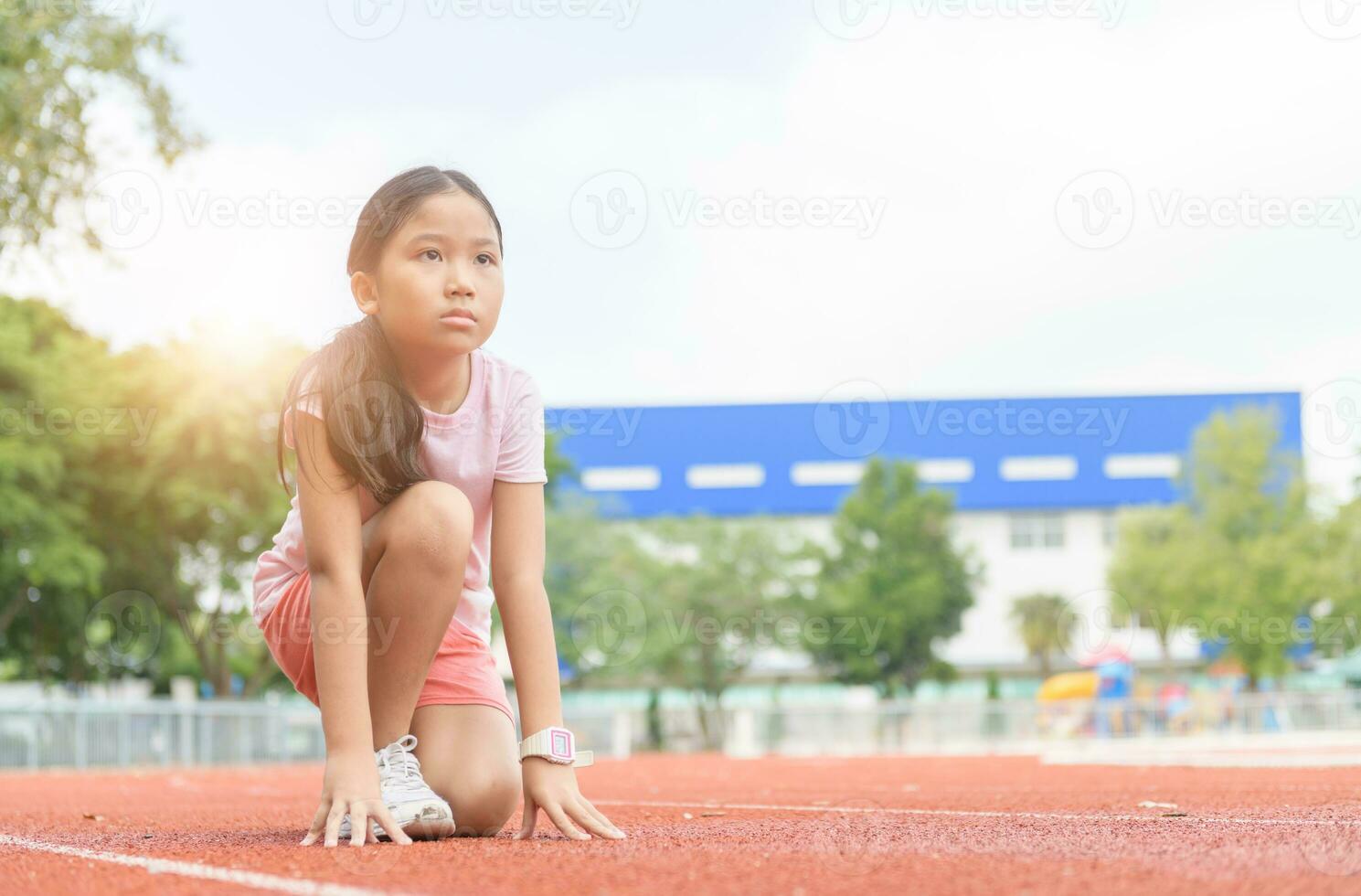 Cheerful cute girl in ready position to run on track, photo