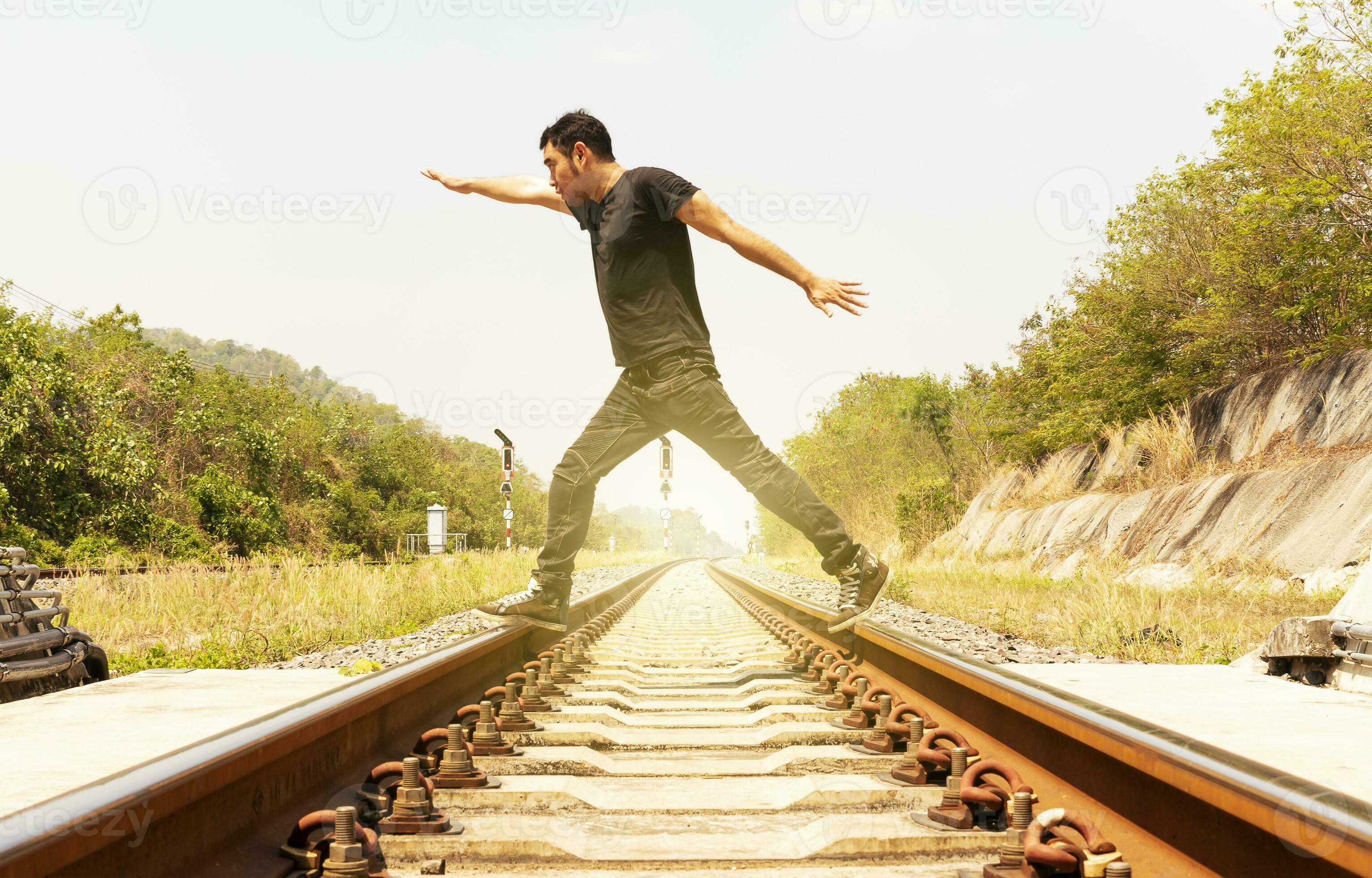 Man wearing black shirt spreads his hands and walk on train tracks
