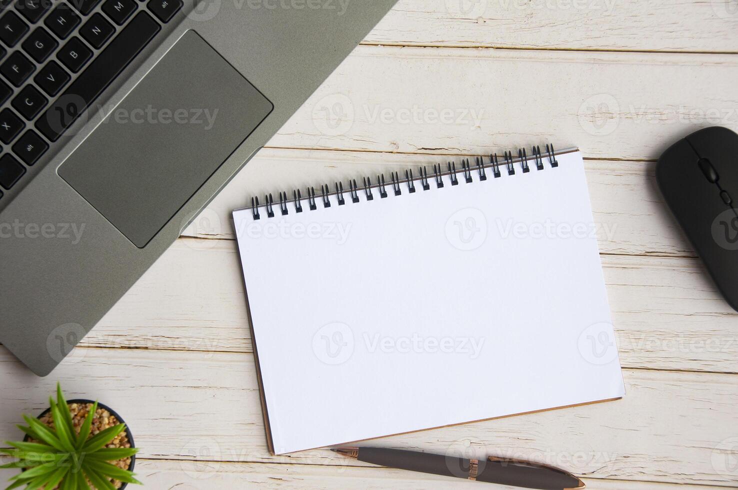 Top view of blank notebook with laptop, table plant and pen background. Copy space photo