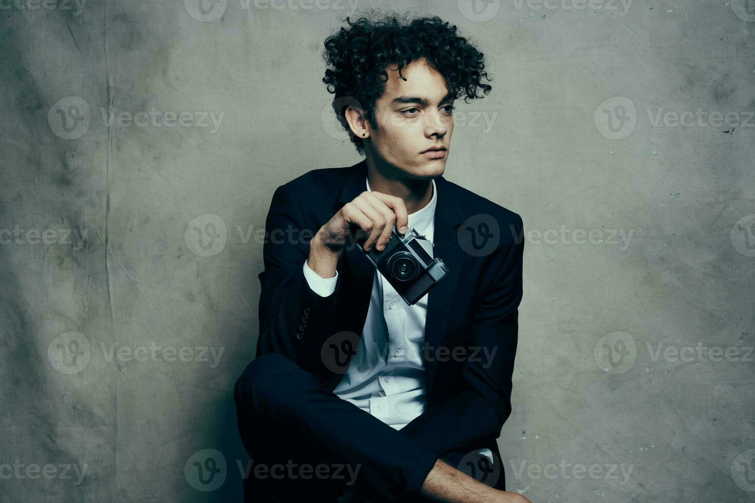 cute guy with curly hair holding a camera in his hand in a studio room model photo