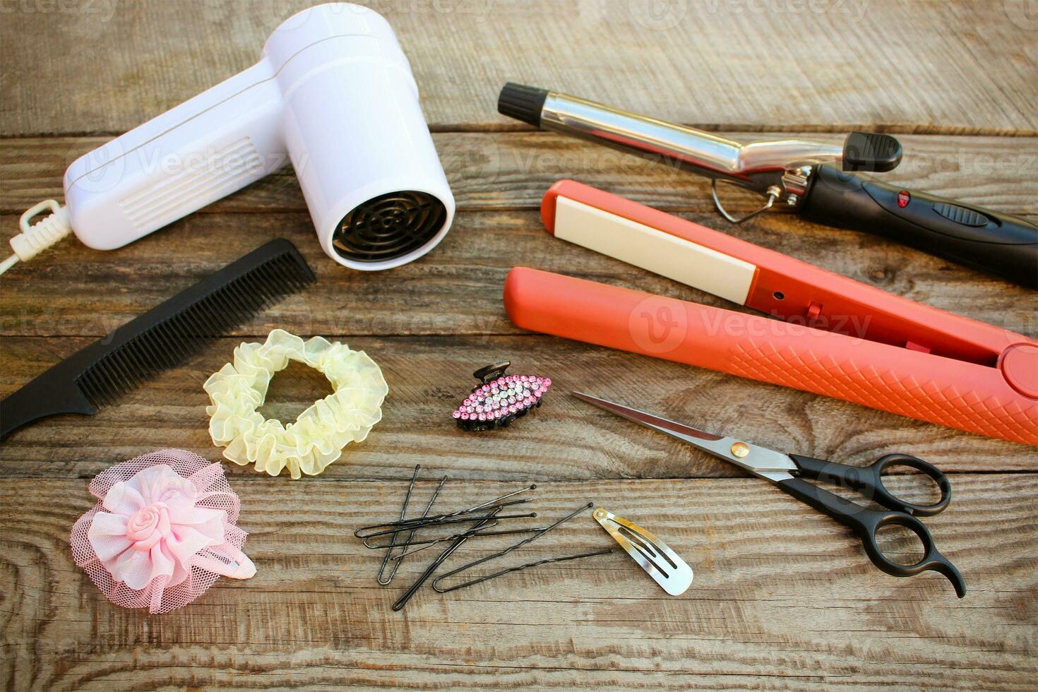 Hair accessories hair dryer, curling iron, hair iron, comb, scissors, hair clips on the old wooden background. Toned image photo