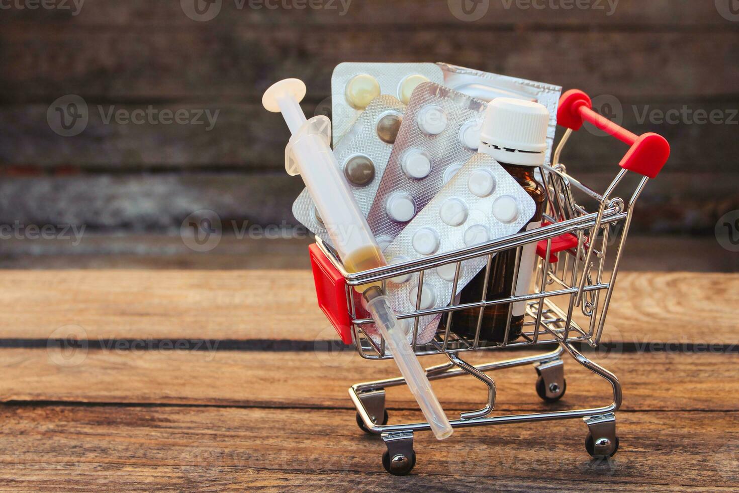 Shopping cart with pills, syringe on the old wood background. Toned image. photo