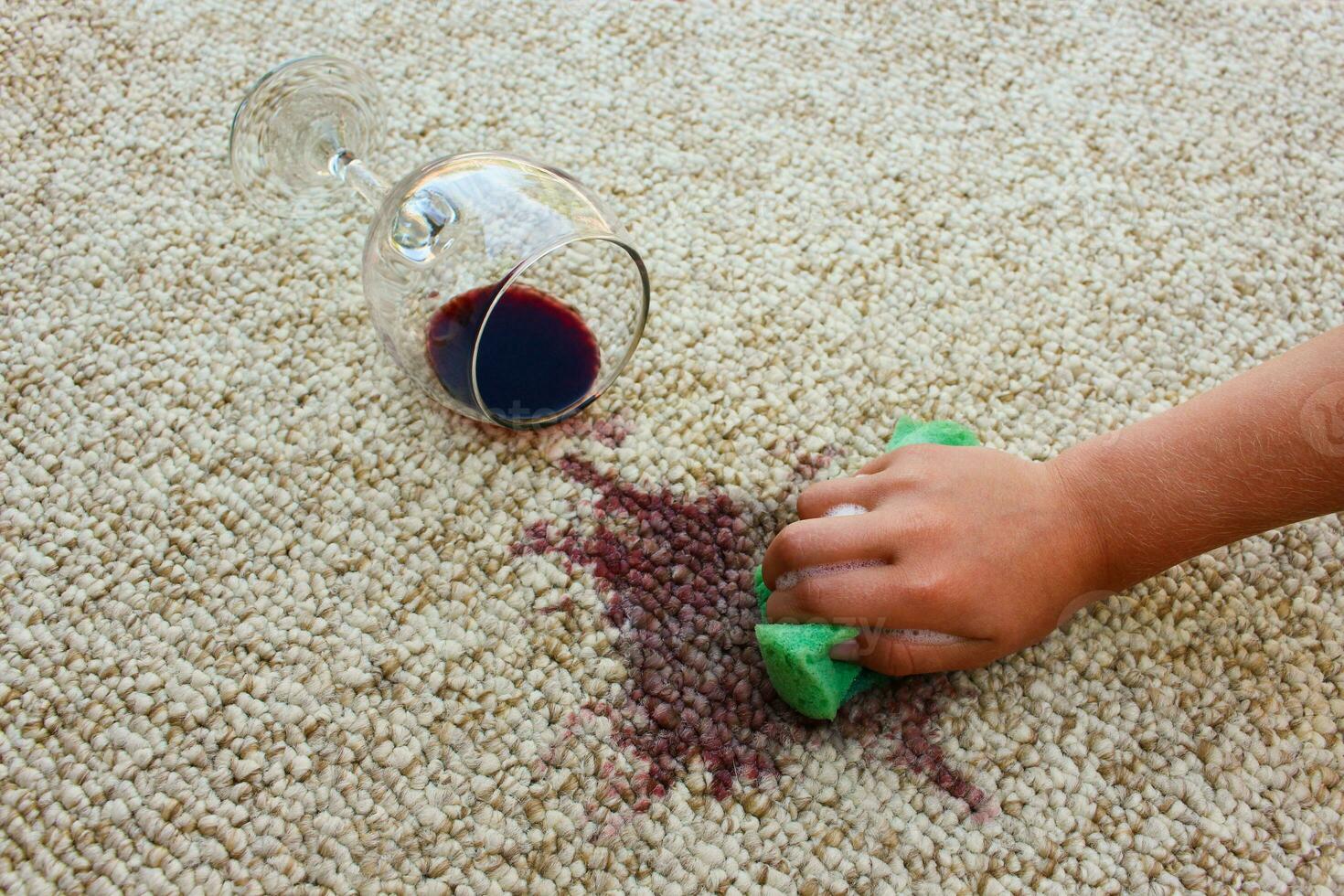 glass of red wine fell on carpet, wine spilled on carpet. Female hand cleans the carpet with a sponge and detergent. photo