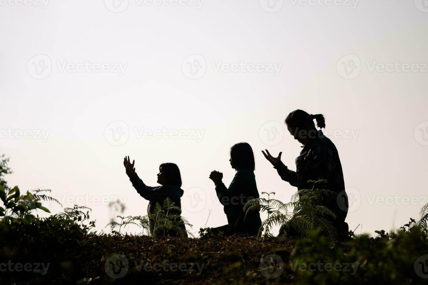 Silhouette of three woman kneeling down praying for worship God at white background. Christians pray to jesus christ for calmness. In morning people got to a quiet place and prayed. copy space. photo