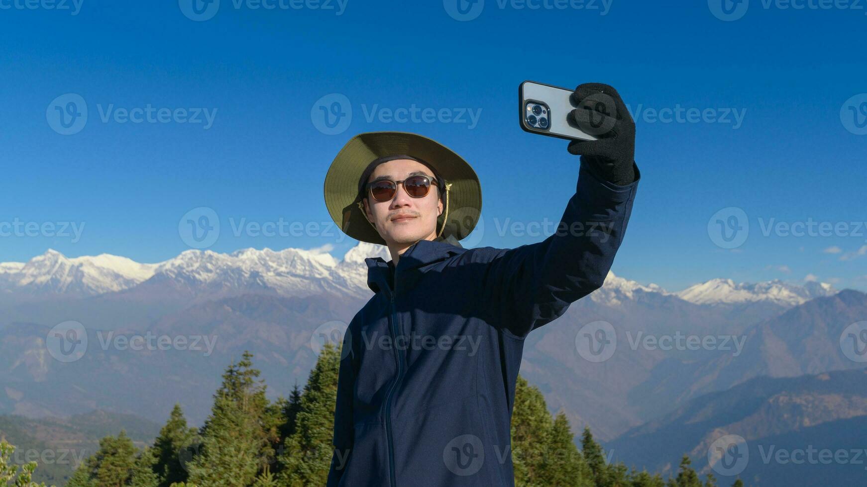 A young traveler takes a selfie or a video call while standing a top a mountain. photo