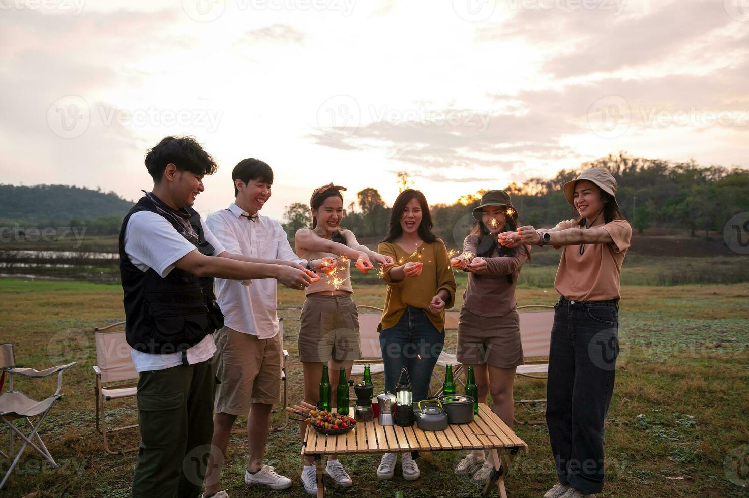 grupo de joven asiático personas son disfrutar cámping , jugando bengala en natural cámping a crepúsculo foto