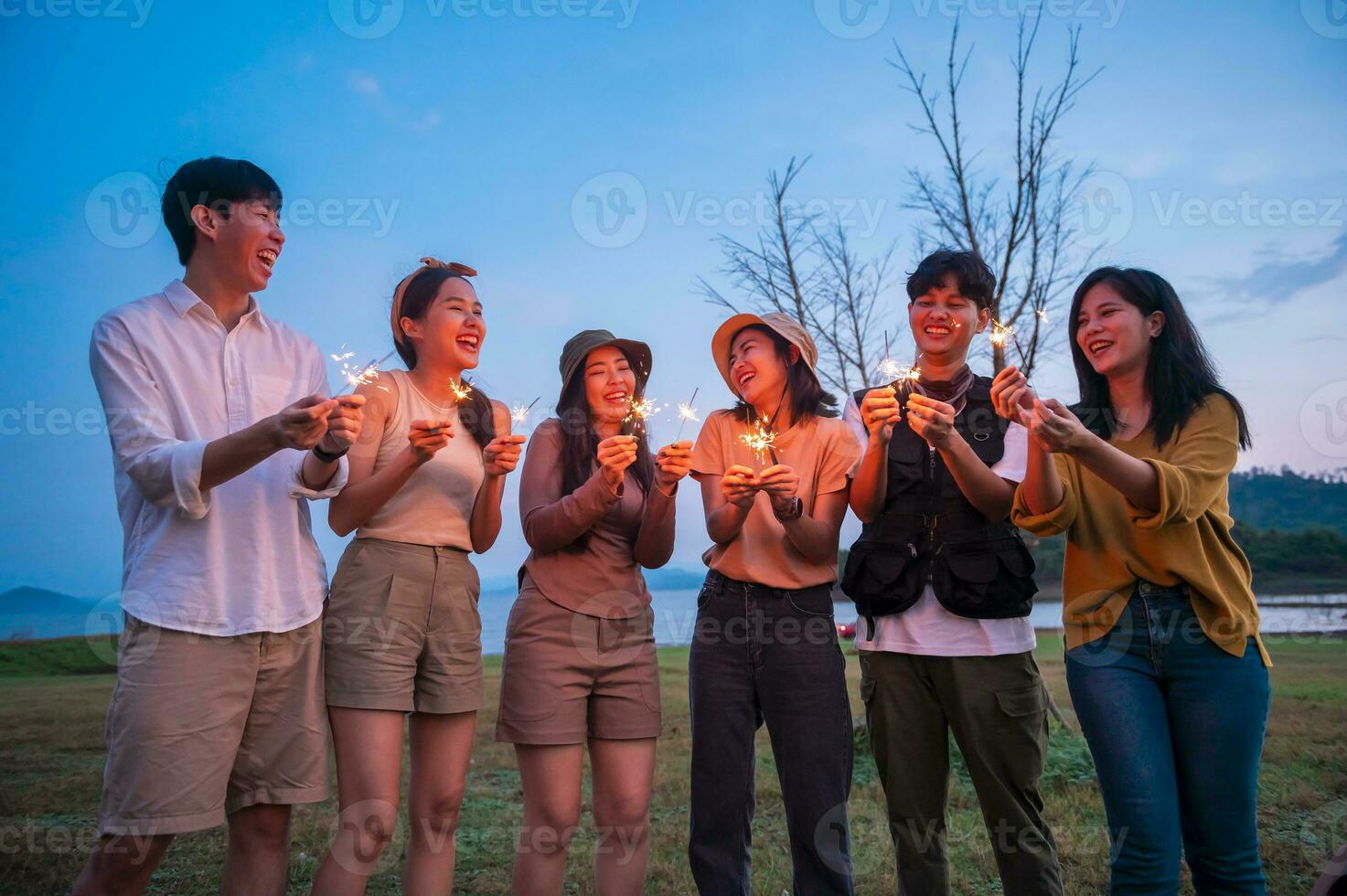 grupo de joven asiático personas son disfrutar cámping , jugando bengala en natural cámping a crepúsculo foto