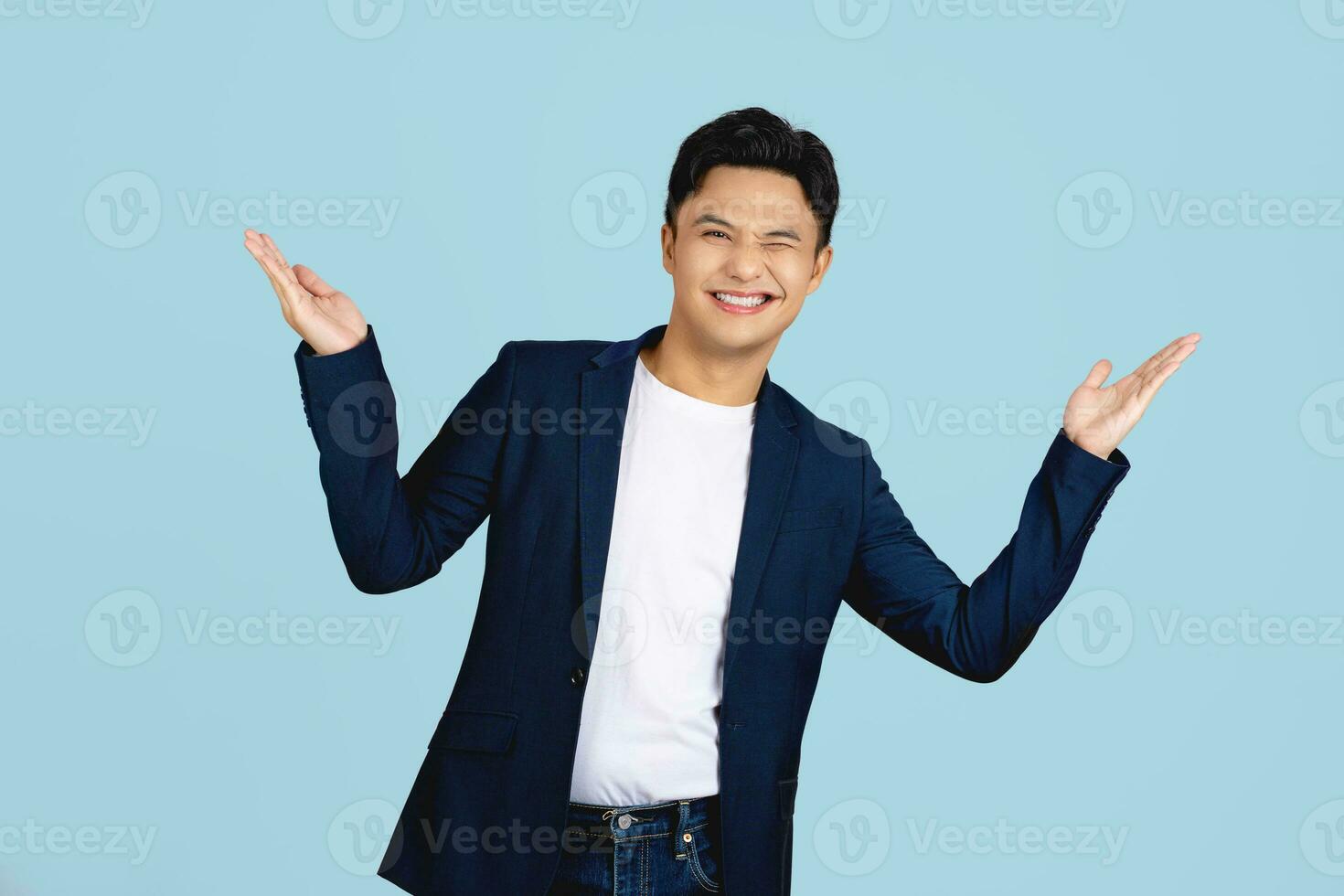 Surprised handsome Asian man in semi formal clothes smiling and opening hands in light blue isolated studio background photo