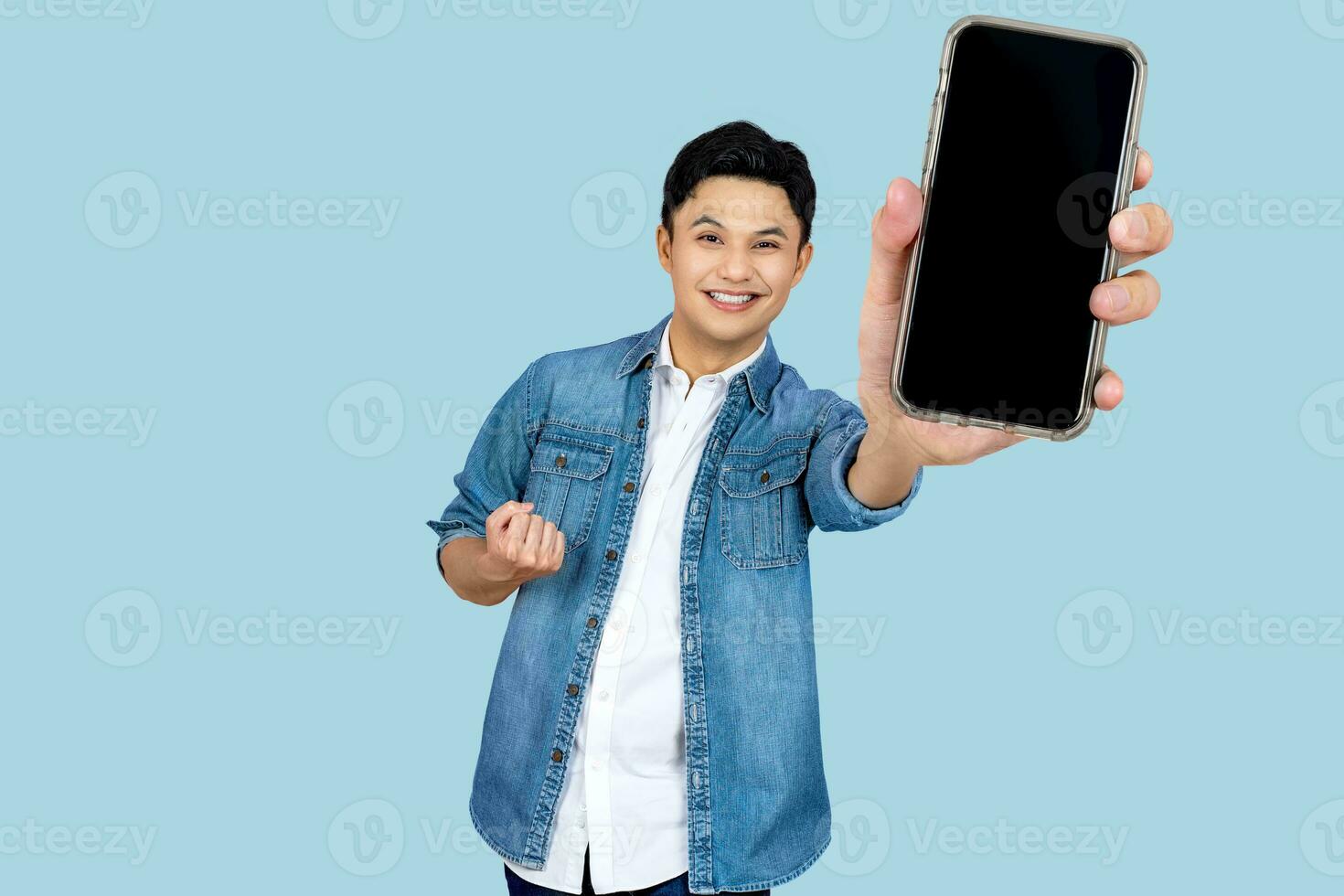 Cheerfull Asian man jumping and smiling in air with showing cellphone blank screen with empty space for mobile app on screen. Isolated in studio light pink background. Creative collage. photo