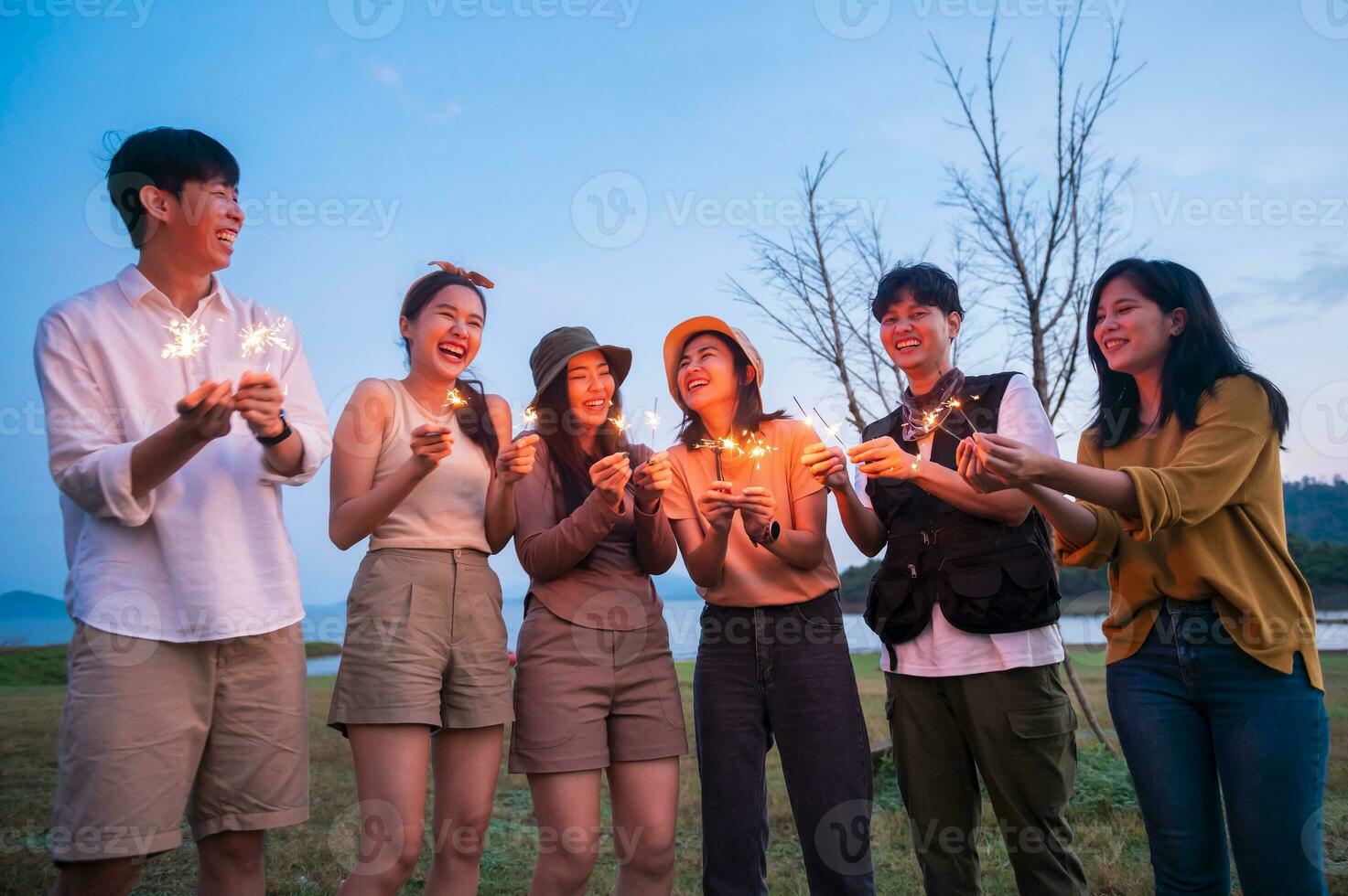 grupo de joven asiático personas son disfrutar cámping , jugando bengala en natural cámping a crepúsculo foto