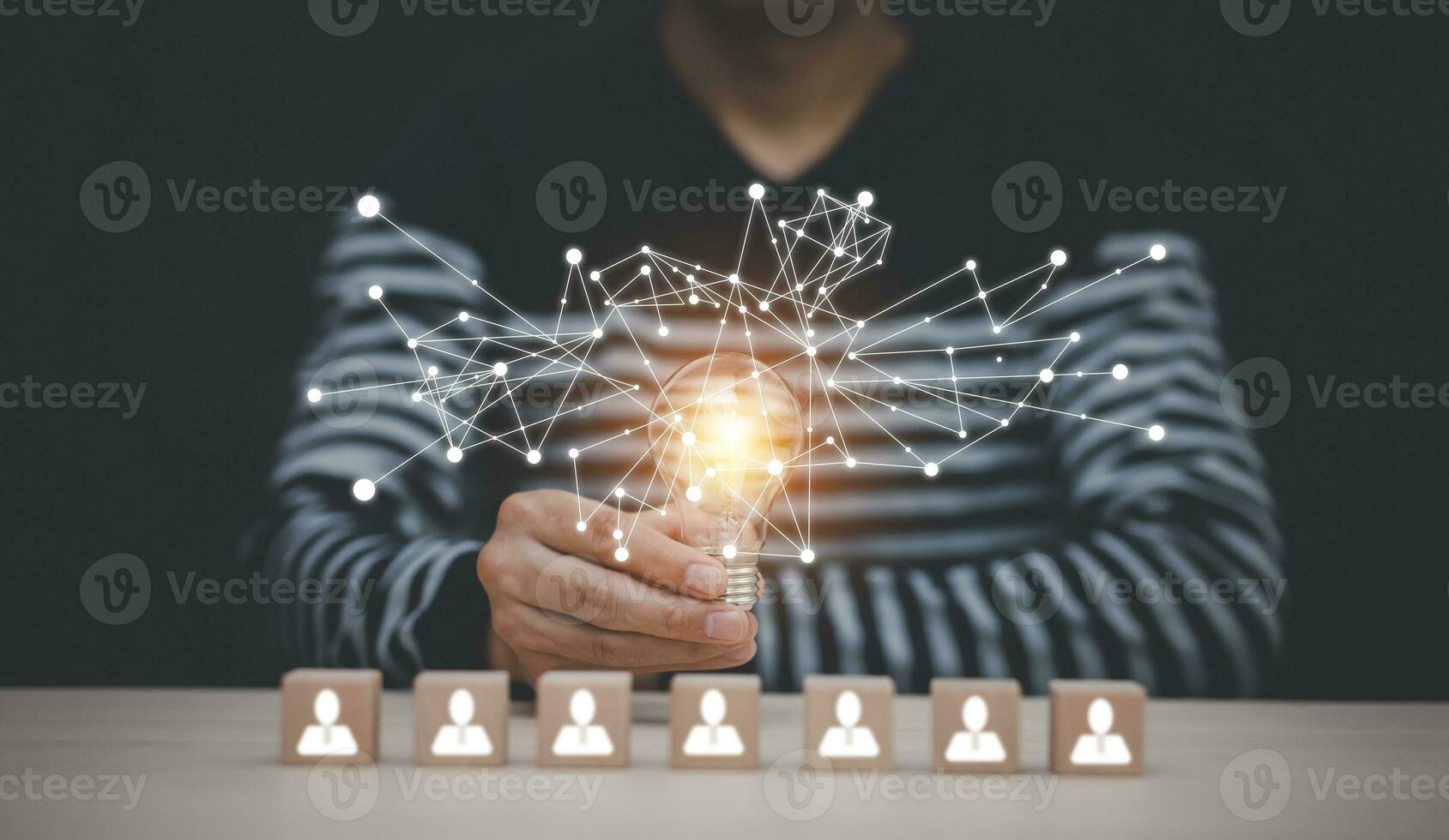 Man hand holding light bulb with Business icon on wood cube and working on desk, Creativity, and innovation are keys to success. Concept of new idea and innovation with Brain and light bulbs. photo