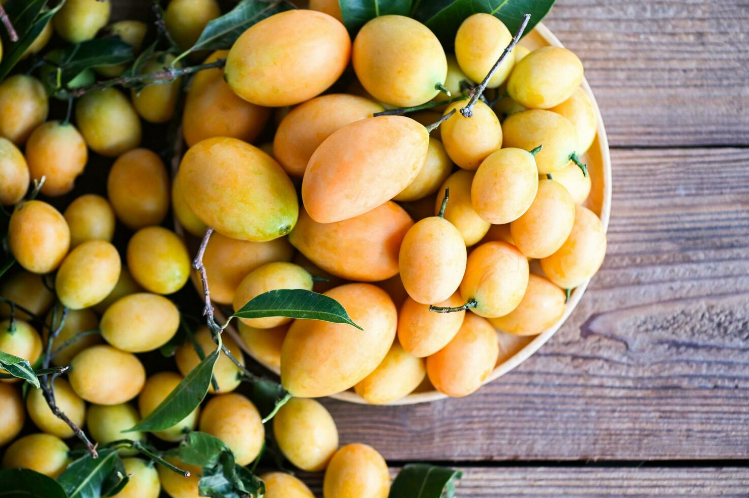 tropical fruit Name in Thailand Sweet Yellow Marian Plum Maprang Plango or Mayong chid, Marian plum fruit and leaves in plate on wooden background photo