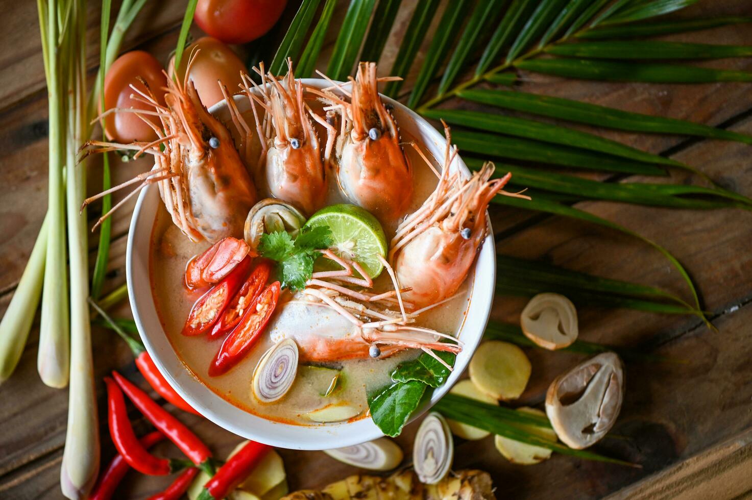 Shrimp soup on seafood soup bowl with thai herb and spices, Thai Food Tom Yum Kung, Hot and sour spicy shrimps prawns soup  curry lemon lime galangal red chili straw mushroom on table food photo