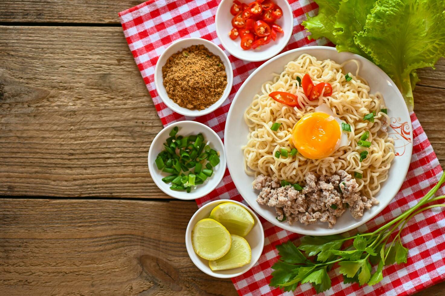 instant noodles cooking tasty eating with bowl - noodle soup, noodles bowl with boiled egg minced pork vegetable spring onion lemon lime lettuce celery and chili on table food photo
