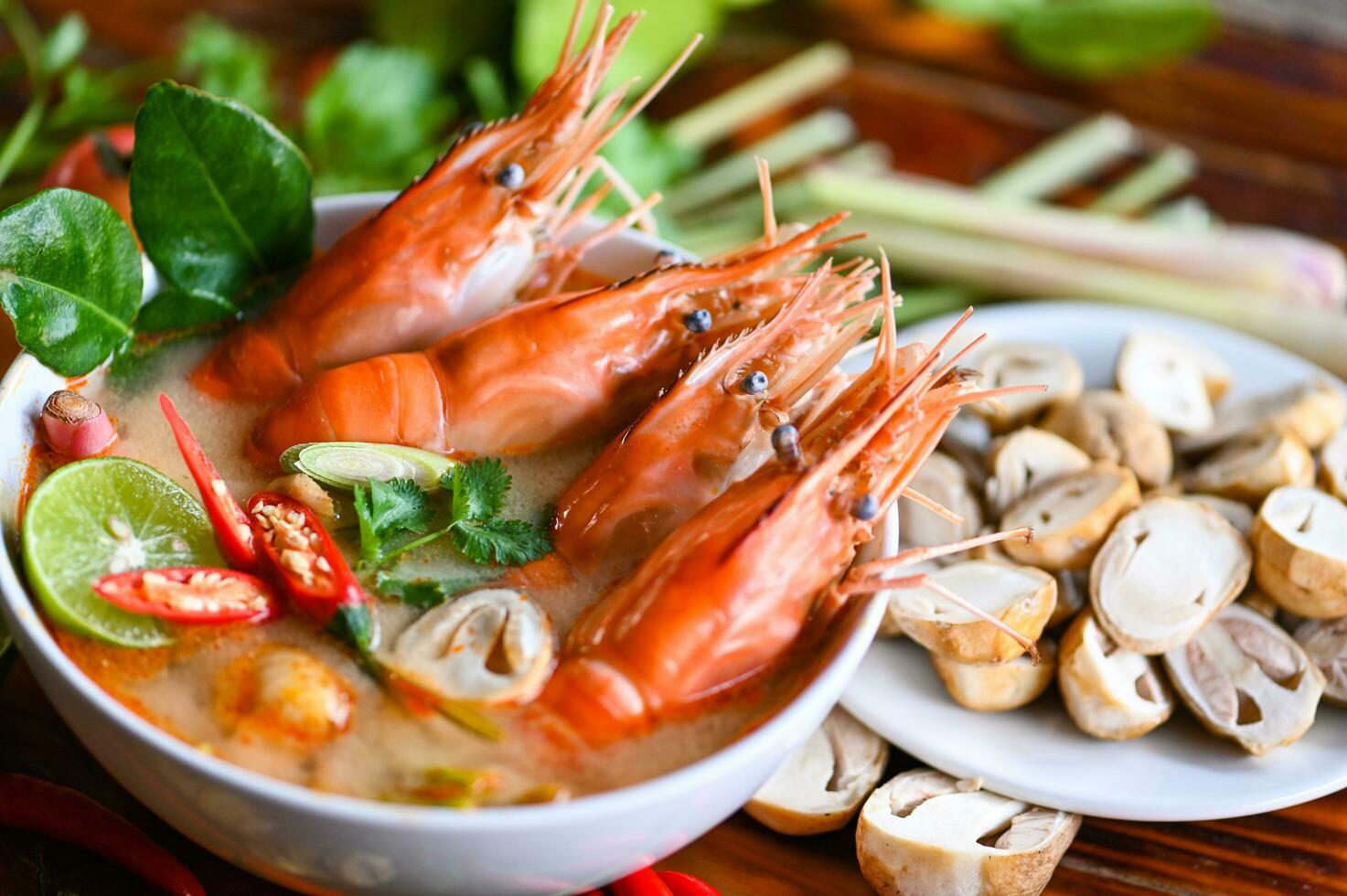 Shrimp soup on seafood soup bowl with thai herb and spices, Thai Food Tom Yum Kung, Hot and sour spicy shrimps prawns soup  curry lemon lime galangal red chili straw mushroom on table food photo