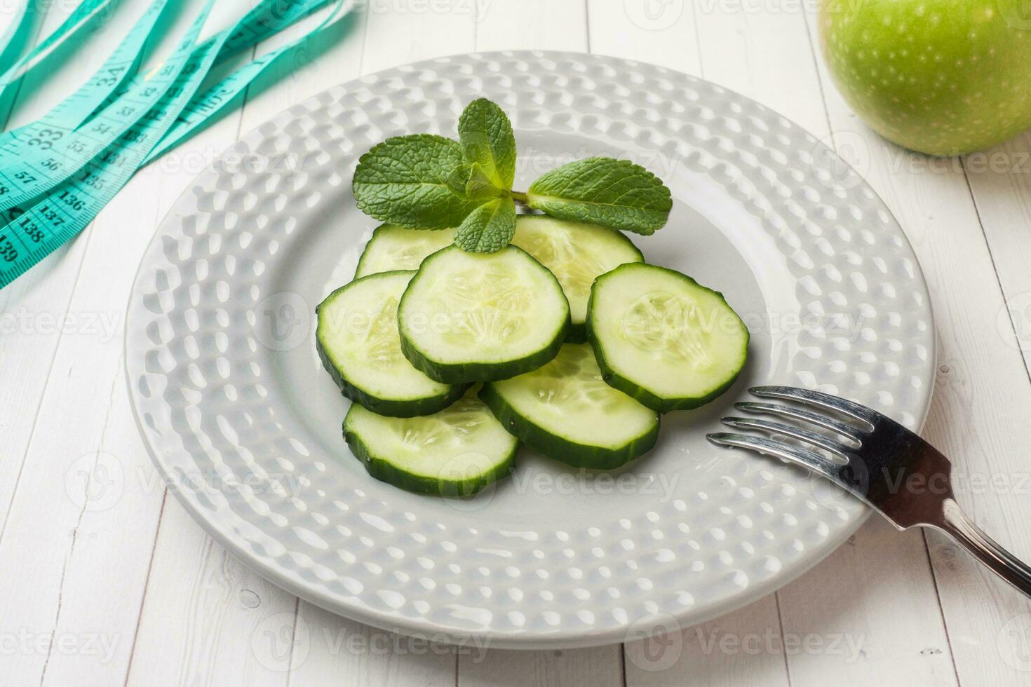 Diet concept. Slides of fresh cucumber on a plate and tape centimeter on a white table. photo