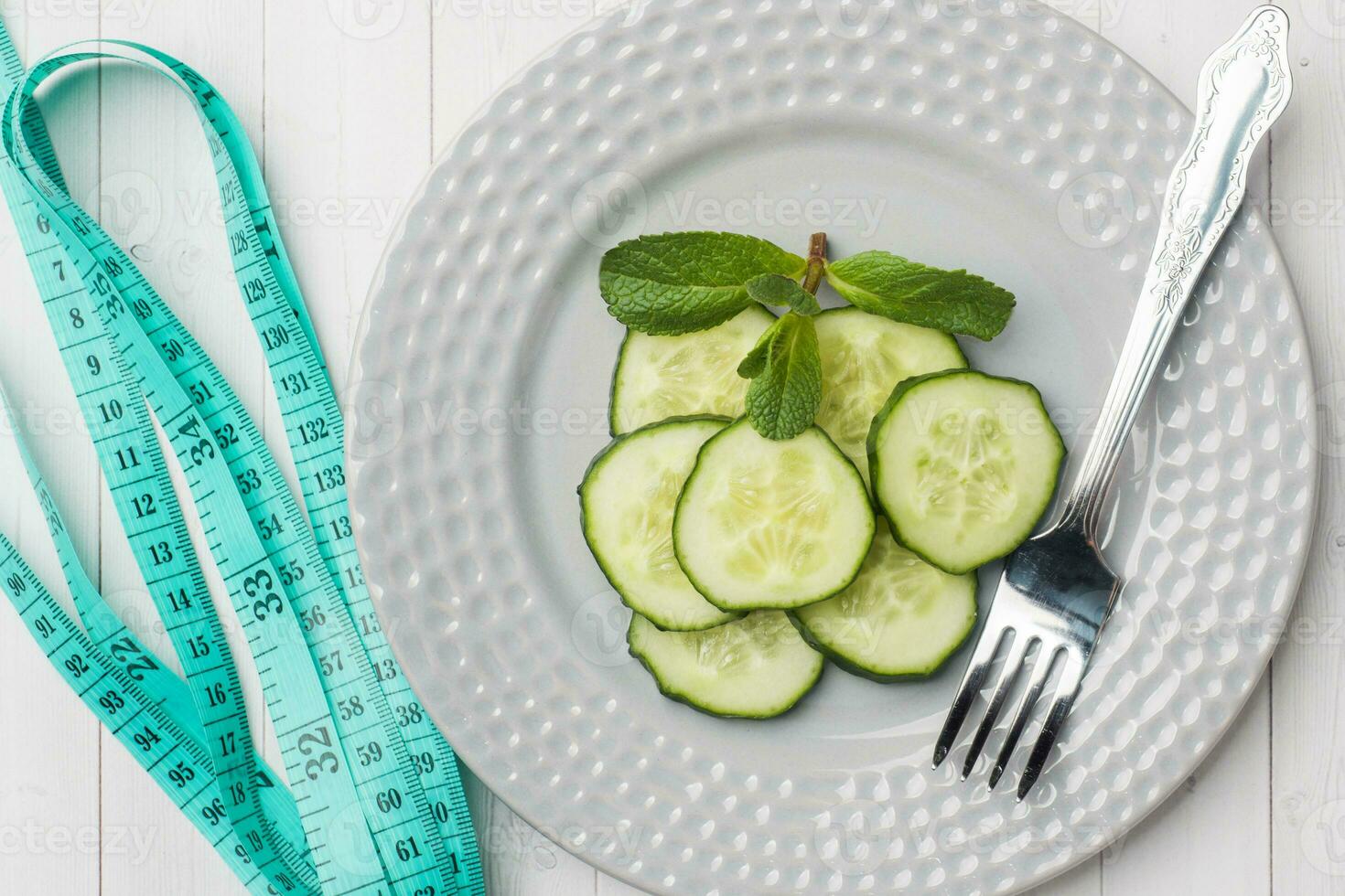 Diet concept. Slides of fresh cucumber on a plate and tape centimeter on a white table. photo