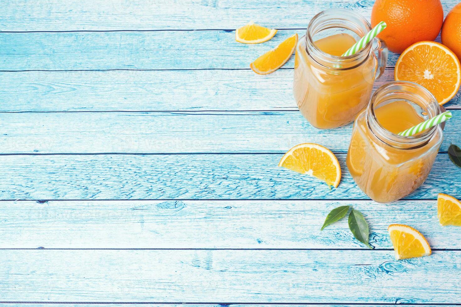 Orange juice in glass jars and fresh oranges on a blue background. photo