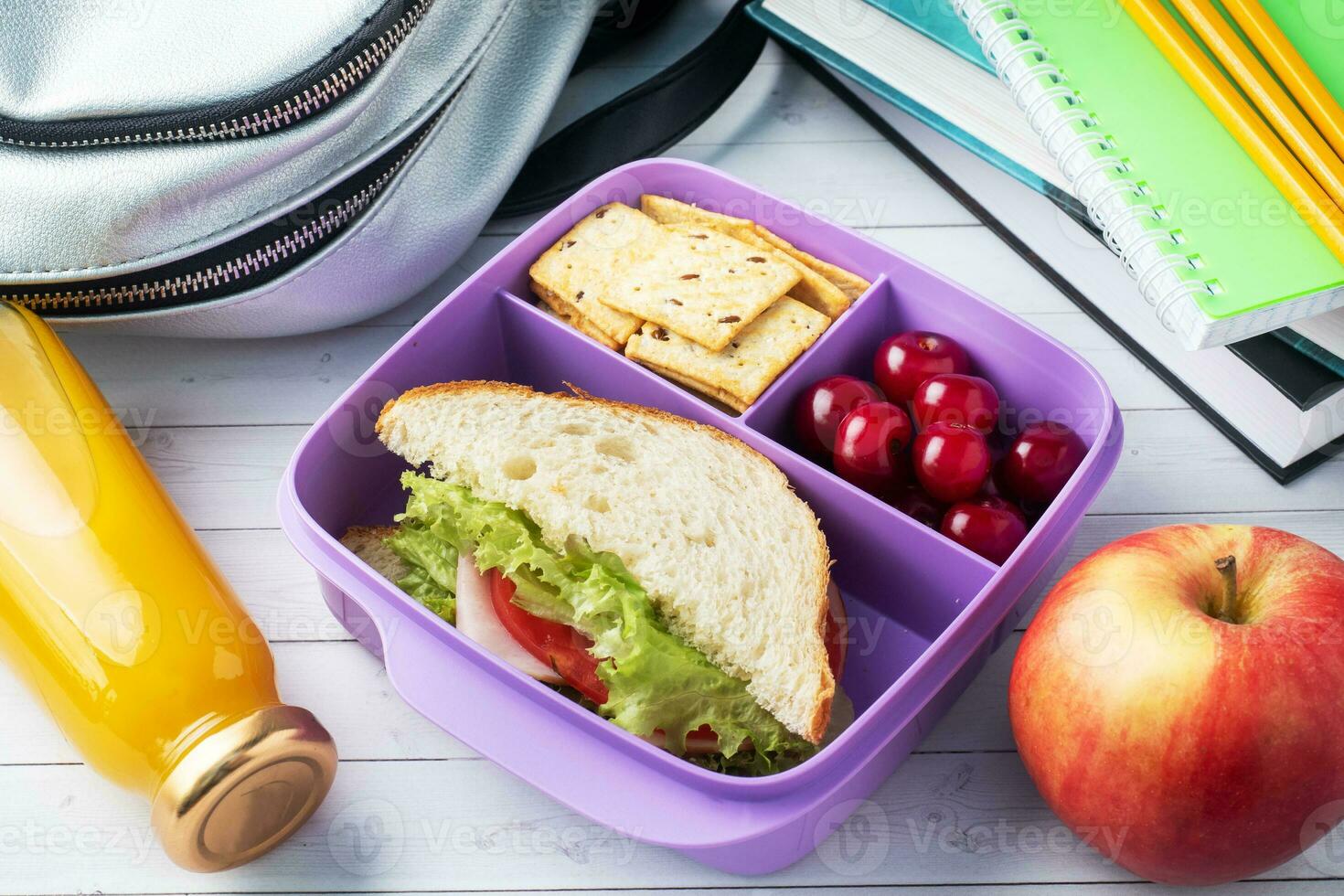 Delicious healthy sandwich in a lunch box, cookies and cherries. Take lunch with you to school or the office. Juice in a bottle and an apple. photo