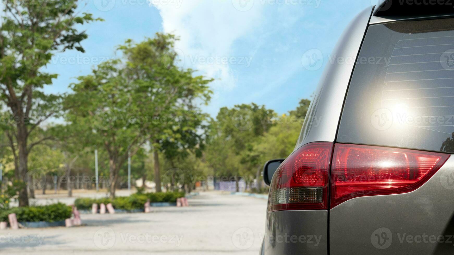 Rear side of gray car. Close up of car tail light. Driving on the soil road with nature of trees in the garden. Background of trees for background under the blur sky. photo