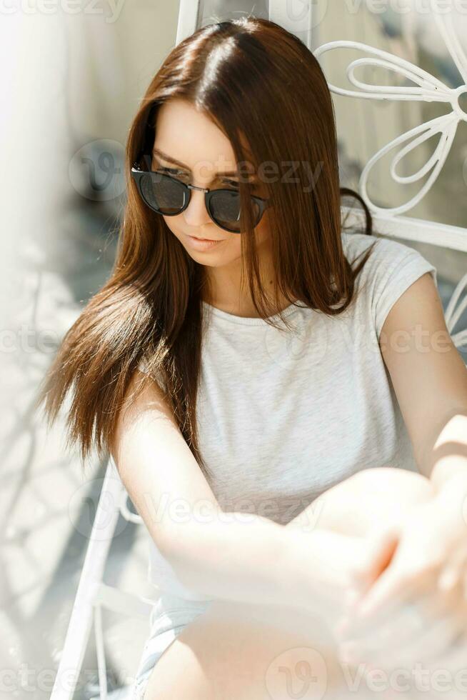 Portrait of beautiful sexy girl in sunglasses sitting in a chair on a sunny day photo