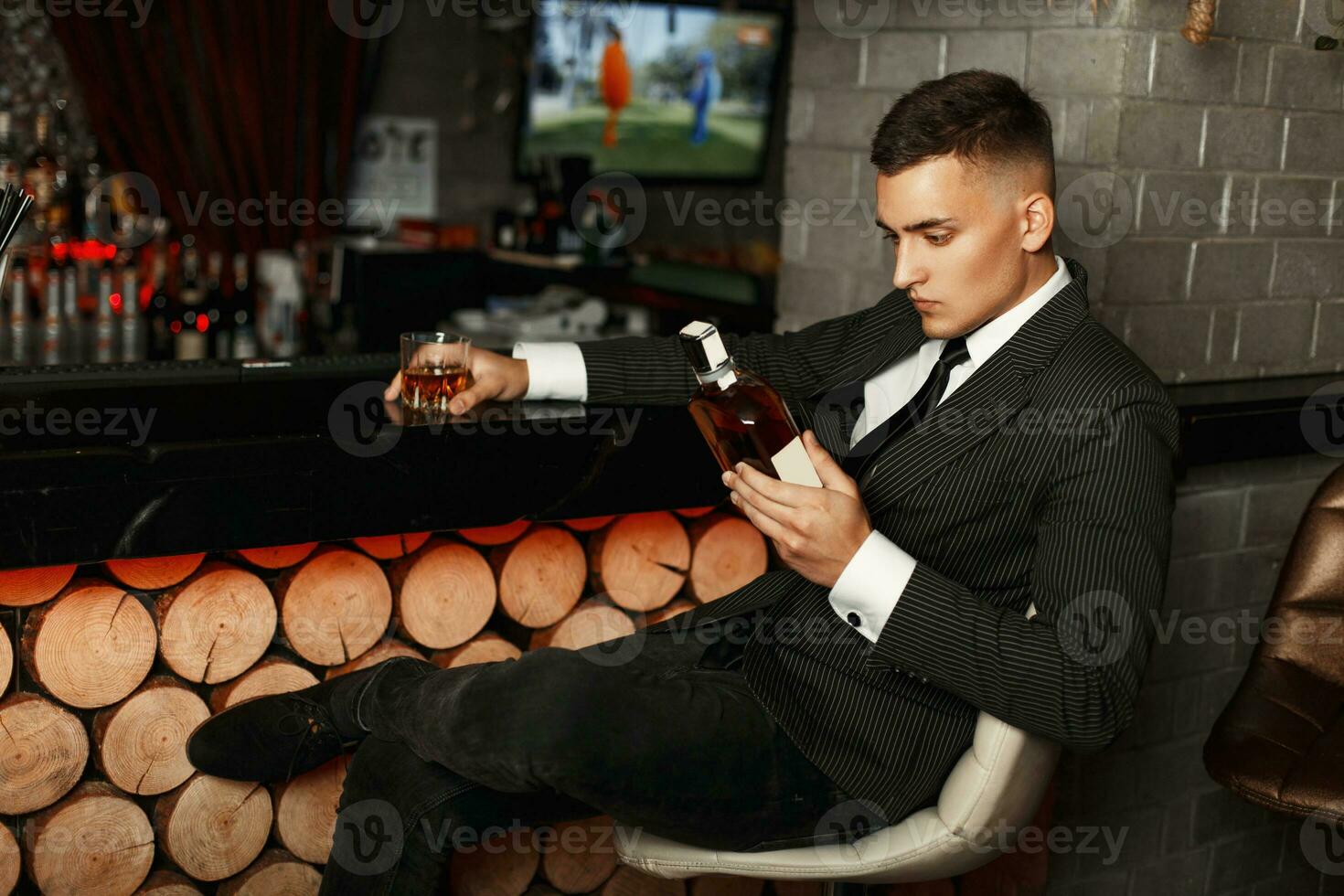 Handsome young man in a stylish suit holding a bottle of whiskey at the bar. photo