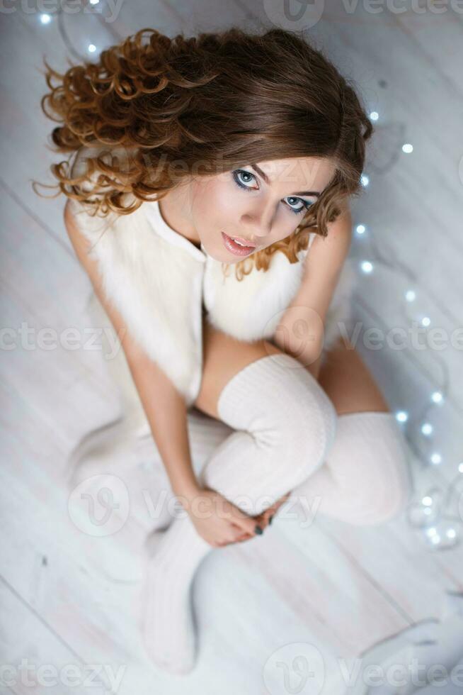 Young beautiful girl in a warm vest and knitted socks sitting on the floor against a background of lights. Top view photo