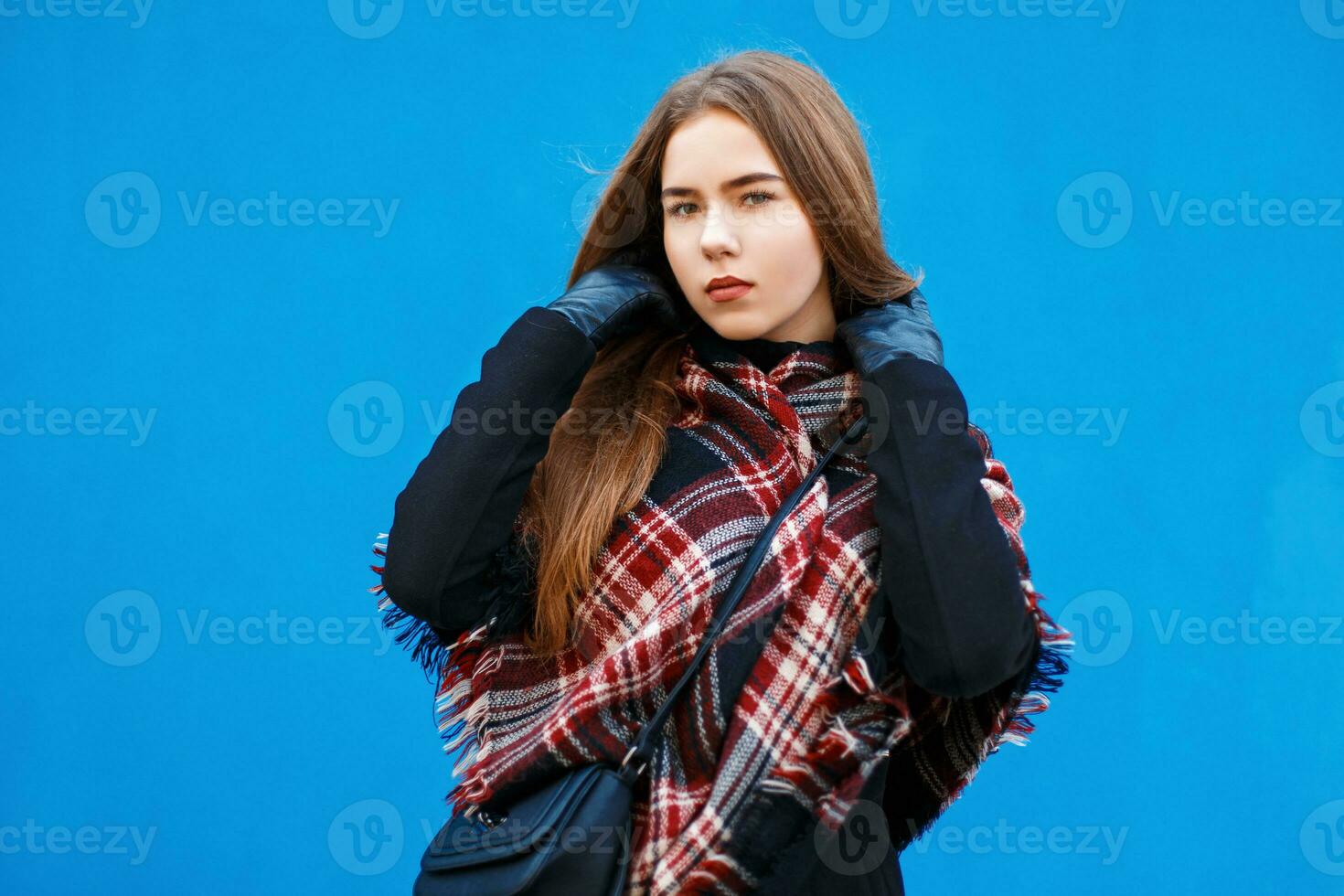Beautiful woman with a scarf and coat posing near a bright blue wall photo