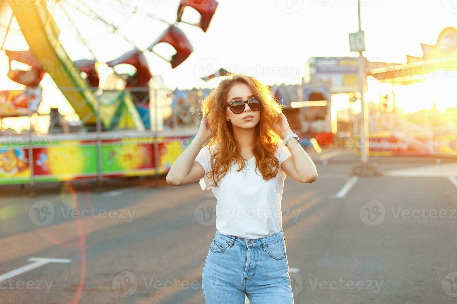Young beautiful girl with bright red hair standing in the amusement park on a summer day at sunset. photo
