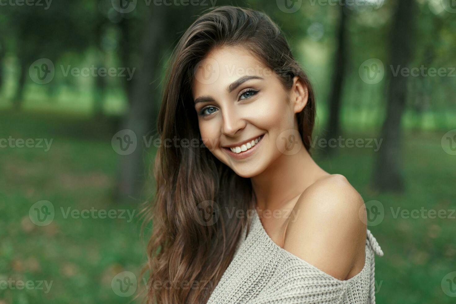 Beautiful happy woman with a cute white smile in a gray knitted sweater in the park photo