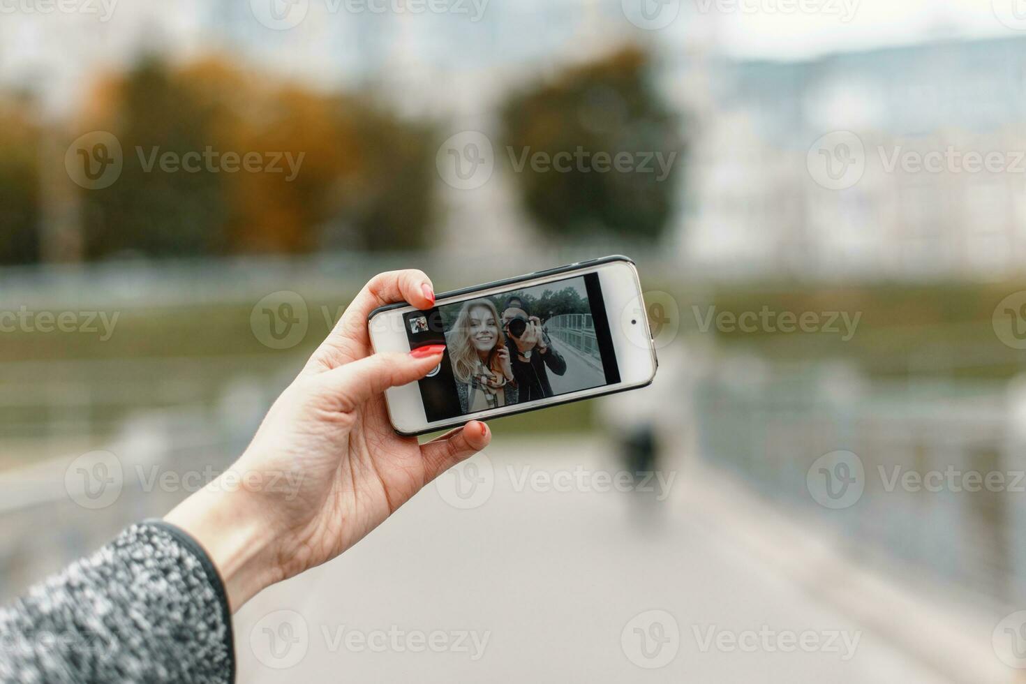 Beautiful girl with friend photographer to take photos on phone